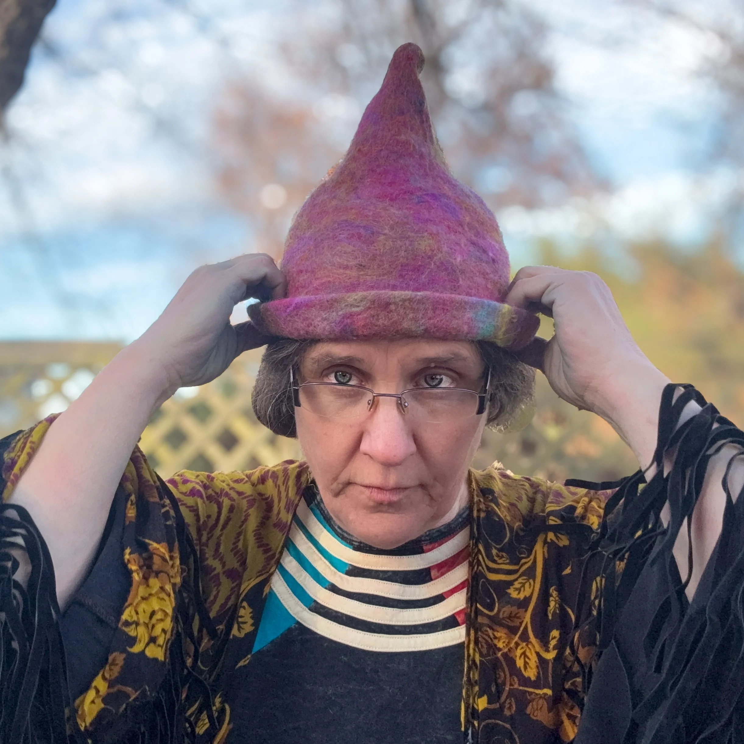 Hand-felted pink trainee witch hat with a bent point and rolled brim, worn by an adult outdoors in soft natural light.