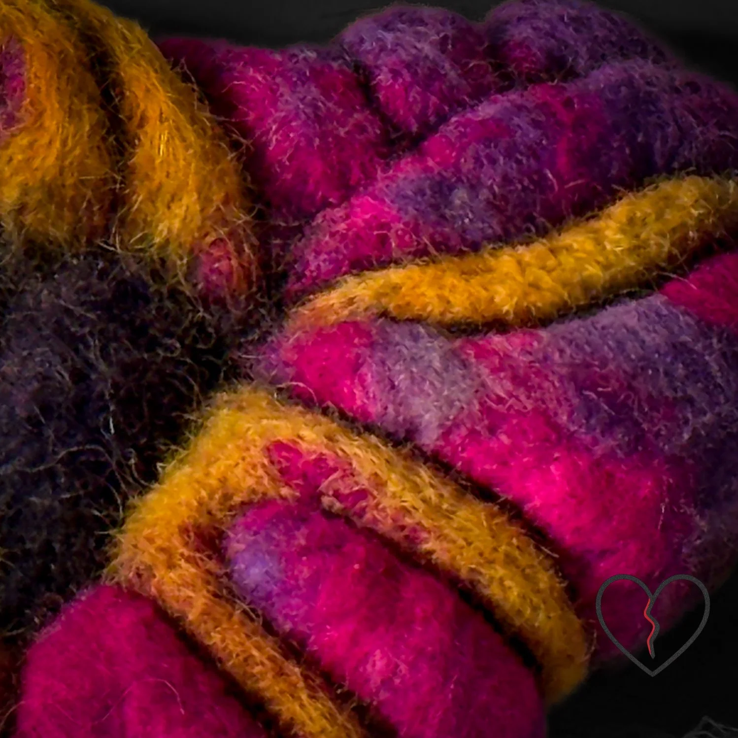 Close-up of textured wool fibers showing flowing cracks and layered color transitions in a broken heart art pin.