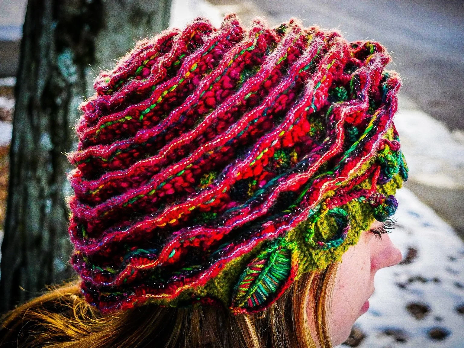 Three-quarter angle shows how The Cosmic Rose wraps around the wearer’s head, emphasizing the dimensional layering of red wool petals and organic flow of the design.