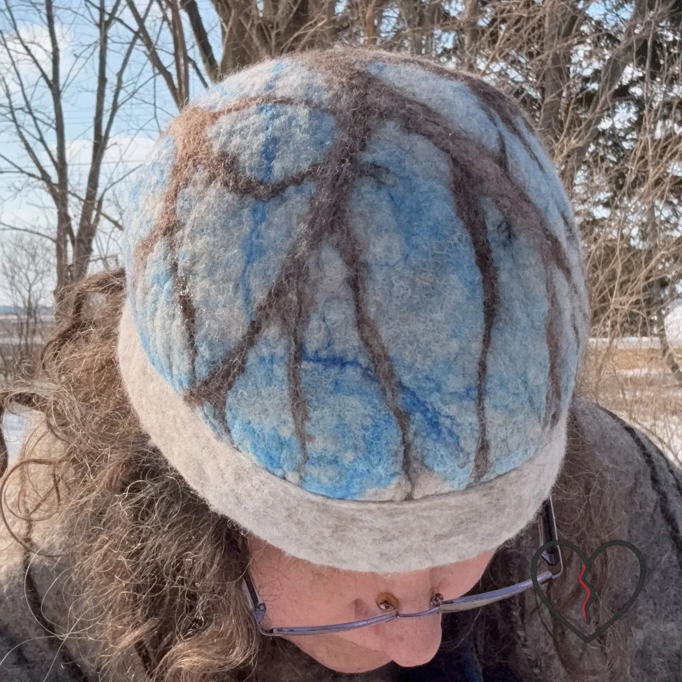 Top view of wet felted wool hat showing blue silk sky pattern and branching brown tree extending across crown, symbolic handmade fiber art hat
