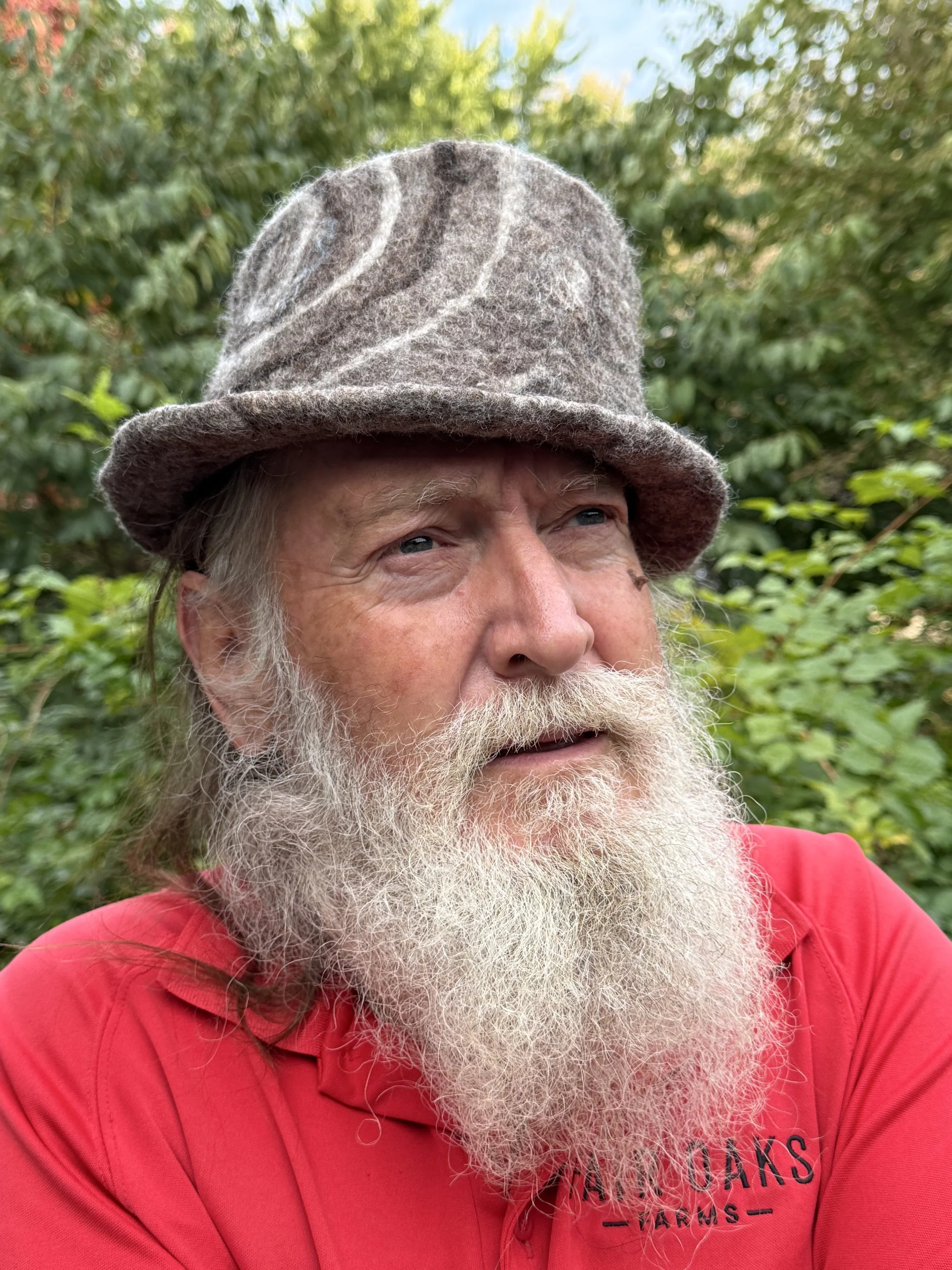 Hand-felted wool fedora hat in natural brown tones with a white and dark brown spiral design, sculptural crown, and short brim, photographed outdoors.