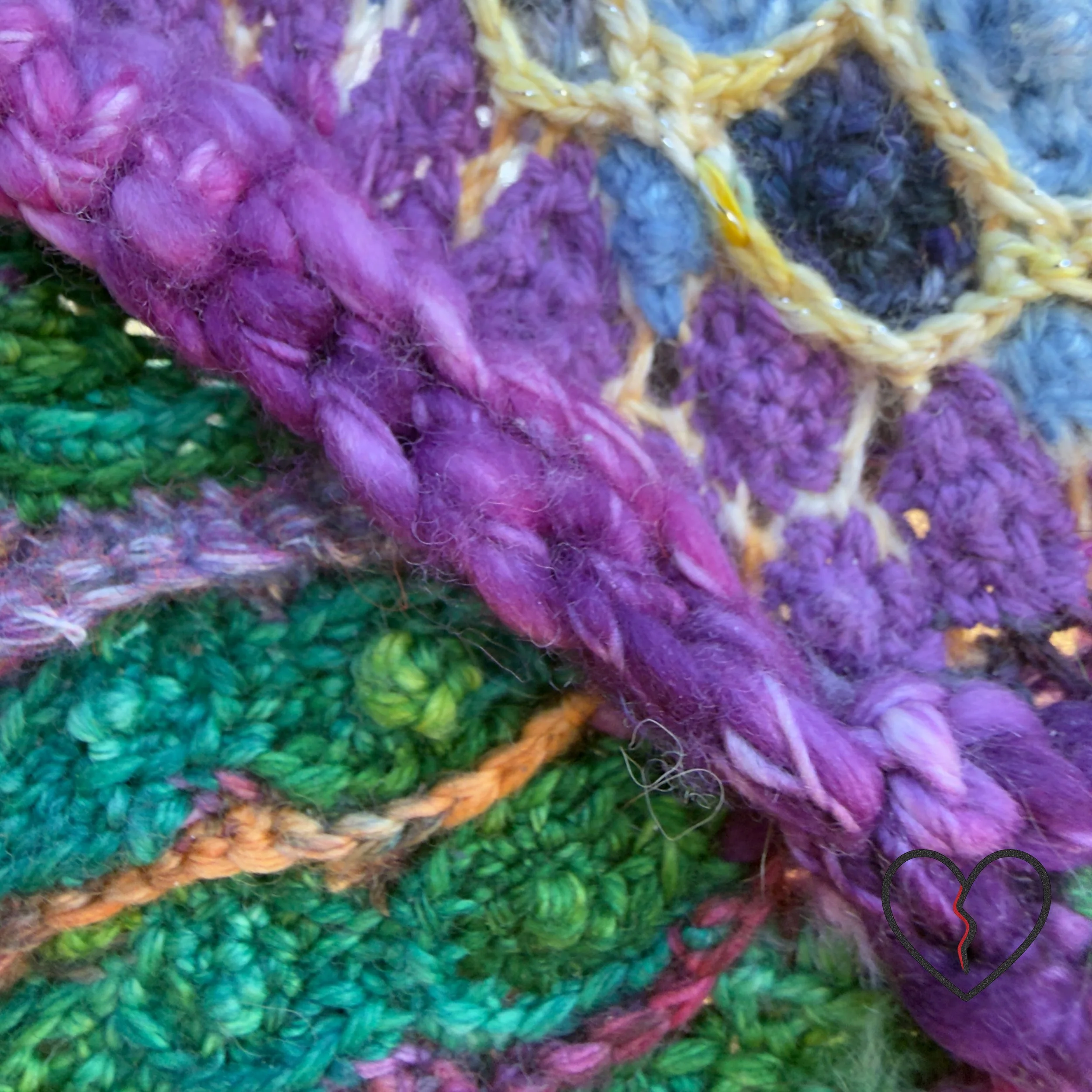 Lower section of a circular crochet wall hanging showing layered green and purple wool stitches arranged in a landscape-like pattern.