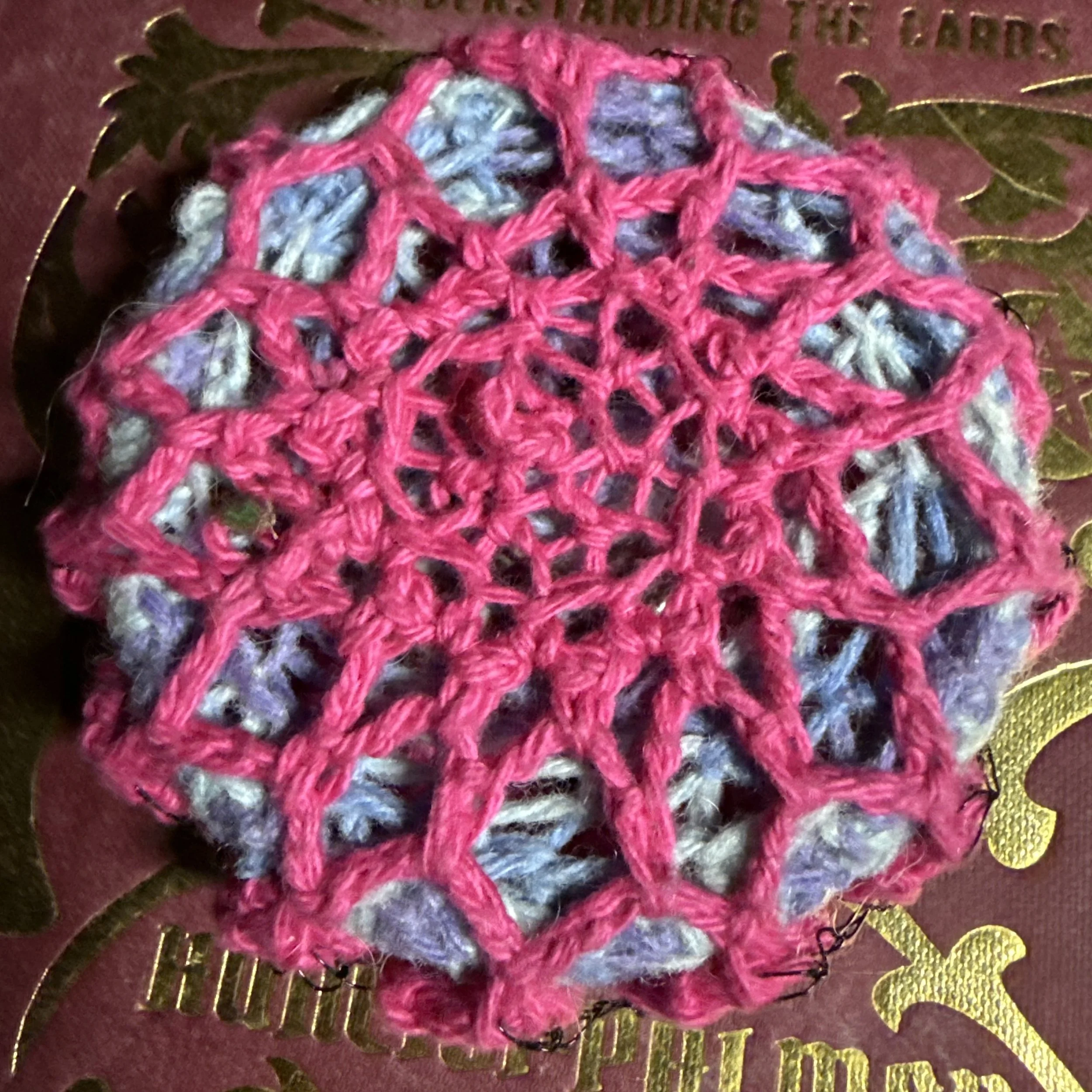 Handmade spiral talisman art pin crocheted with wool, cotton, and black wire around a repurposed bracelet base.