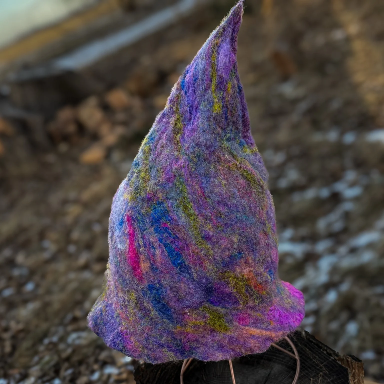 Front view of a tall hand-felted trainee witch hat in purple with subtle blue and green fiber accents.