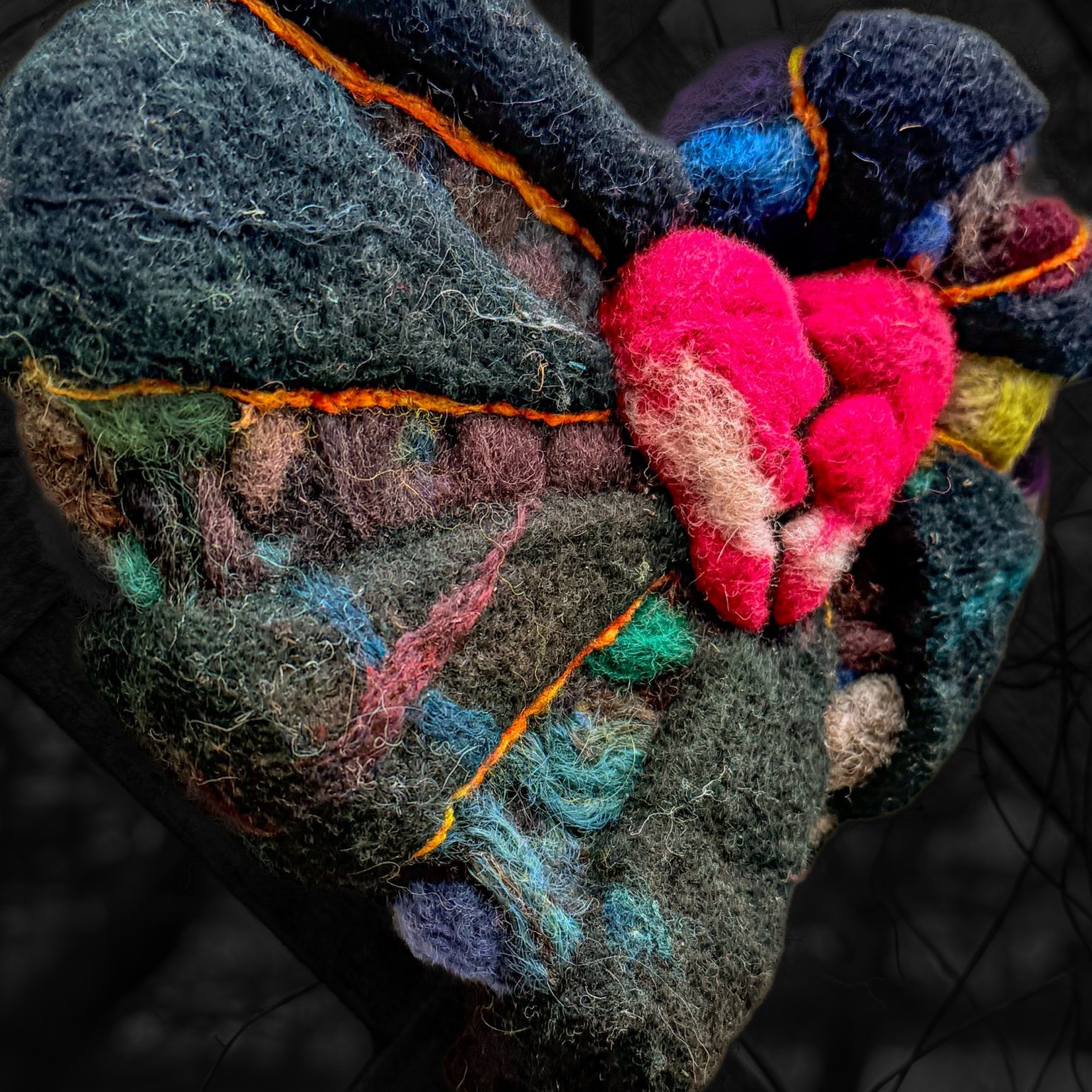 Side view of a felted wool broken heart with layered dark textures.