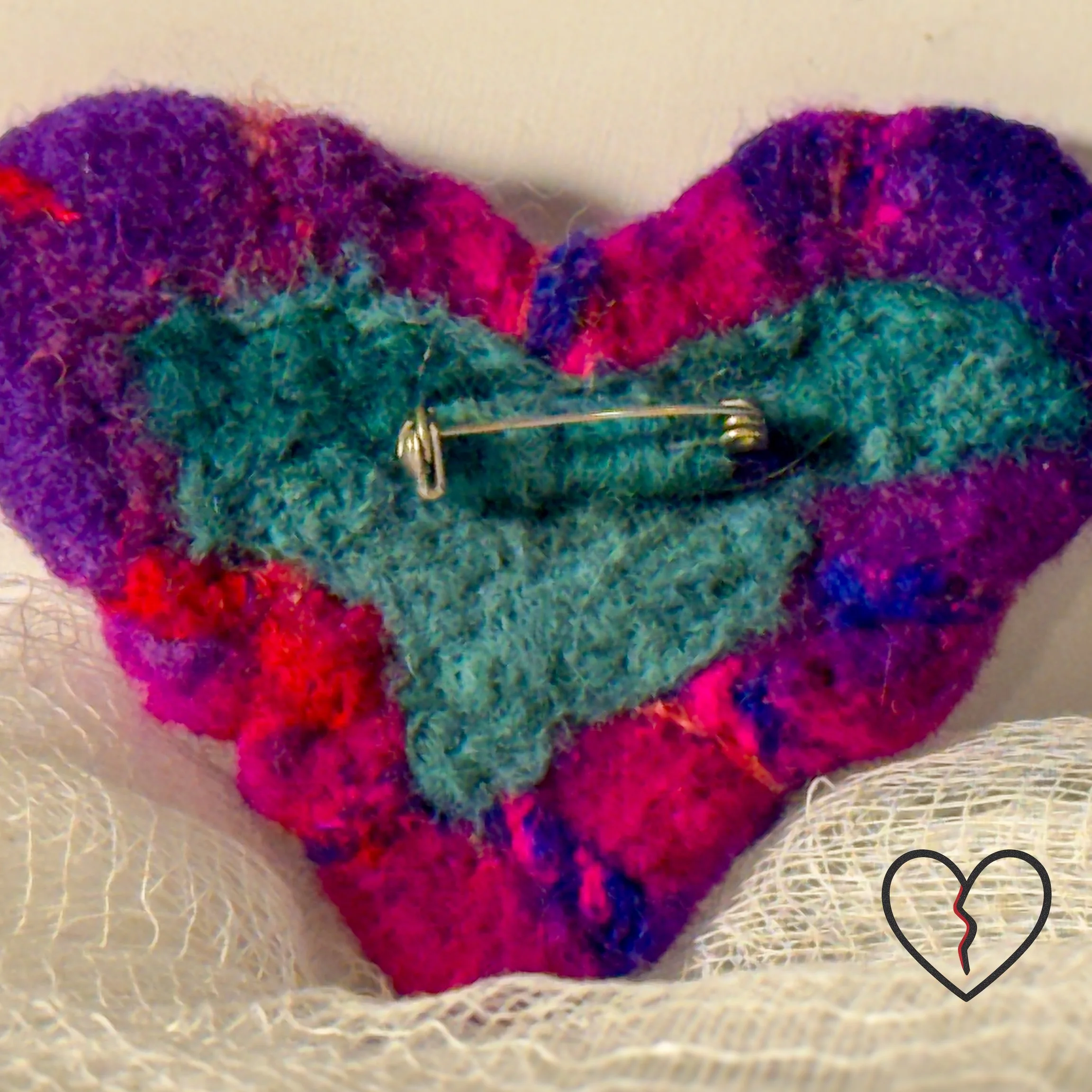 Back of hand-felted wool broken heart pin with teal wool backing and one-inch stainless steel jewelry pin attached.