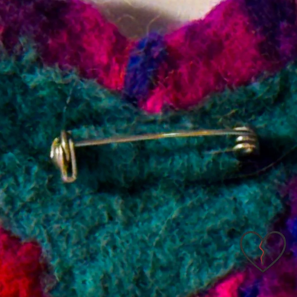 Close-up detail of stainless steel jewelry pin mounted on hand-dyed wool backing of a small broken heart fiber art pin.