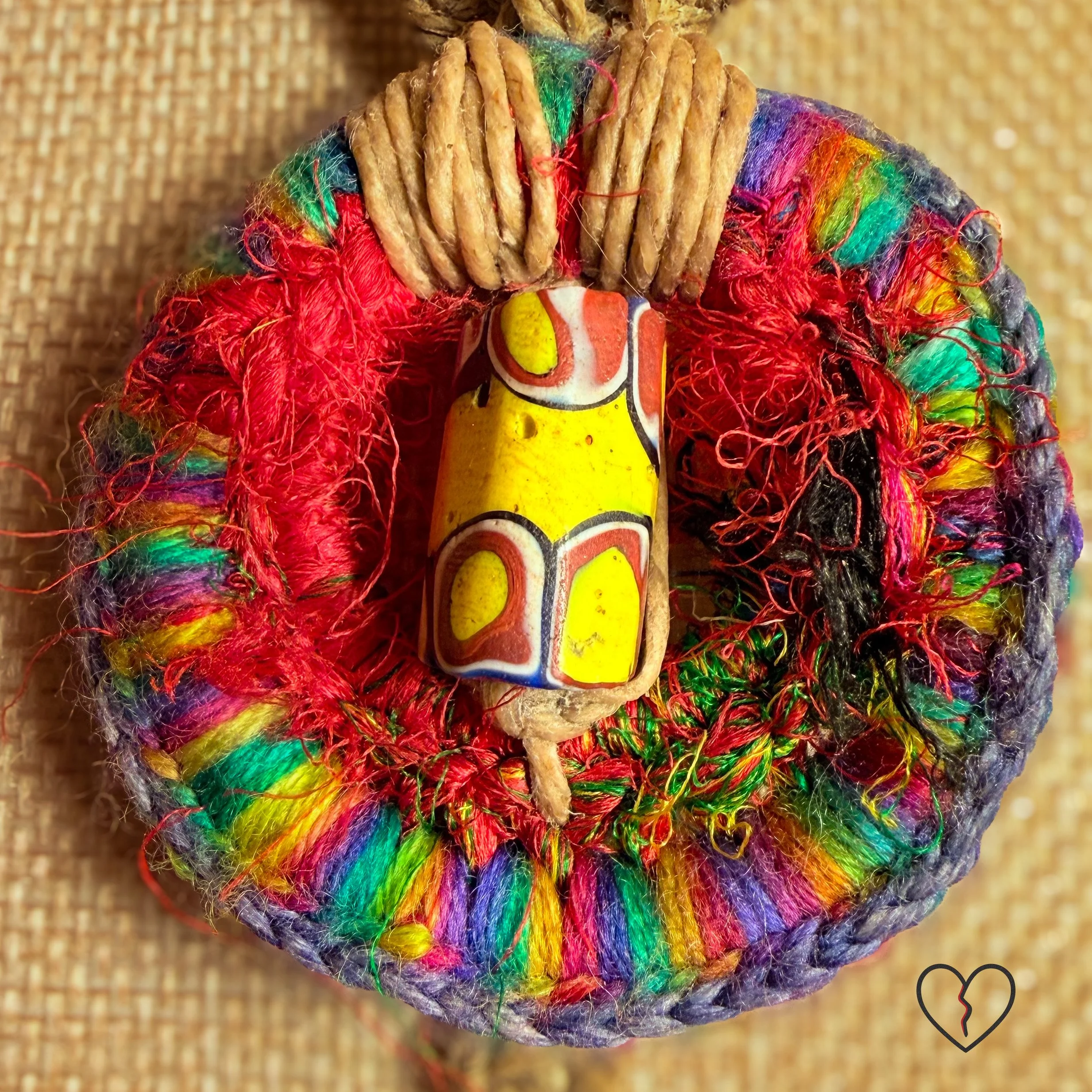 Fiber necklace with yellow trade bead, wool circle, hemp cord, and tassel.