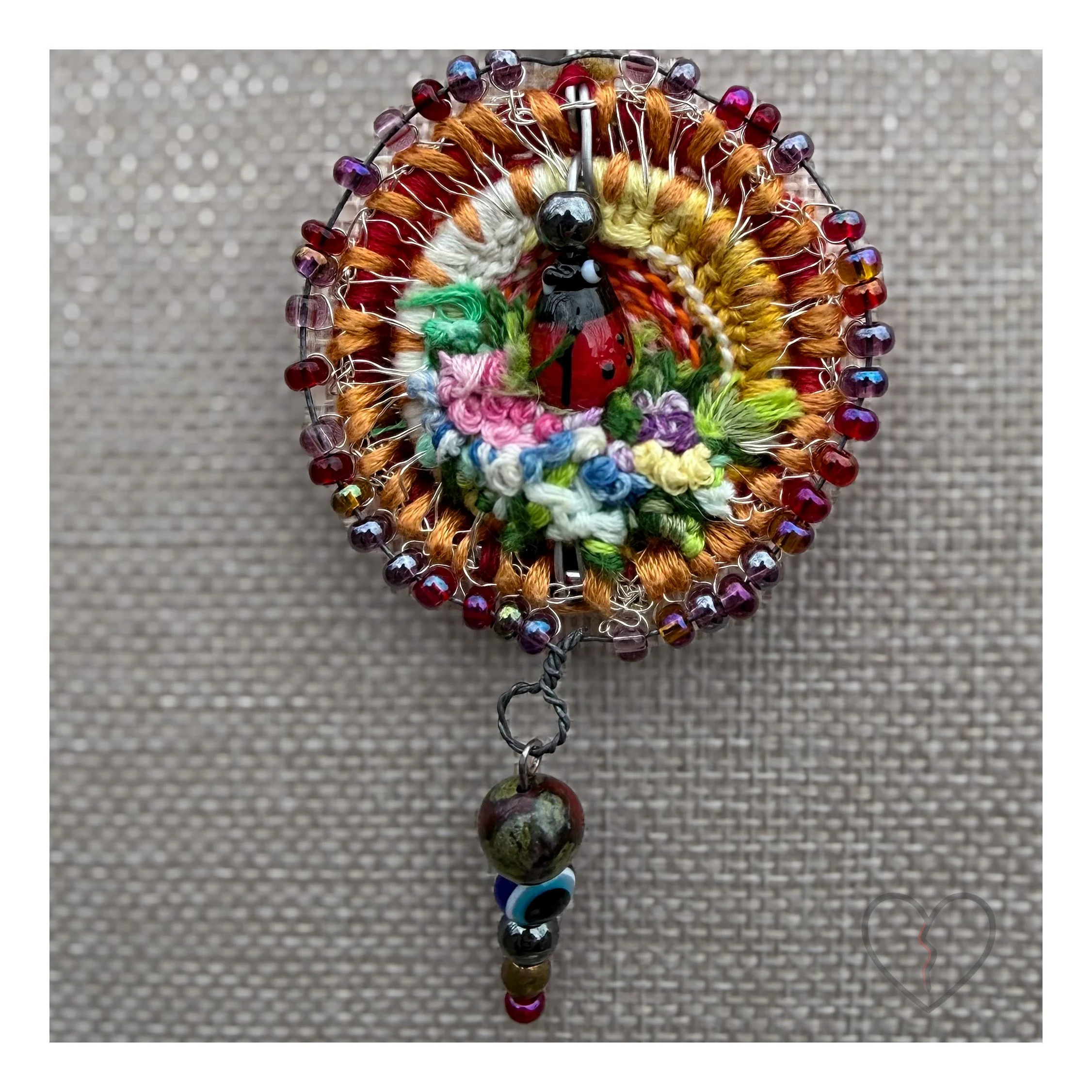 Close up of wool ladybug pendant with textured garden details Circular textile pendant with beadwork and pendulum drop