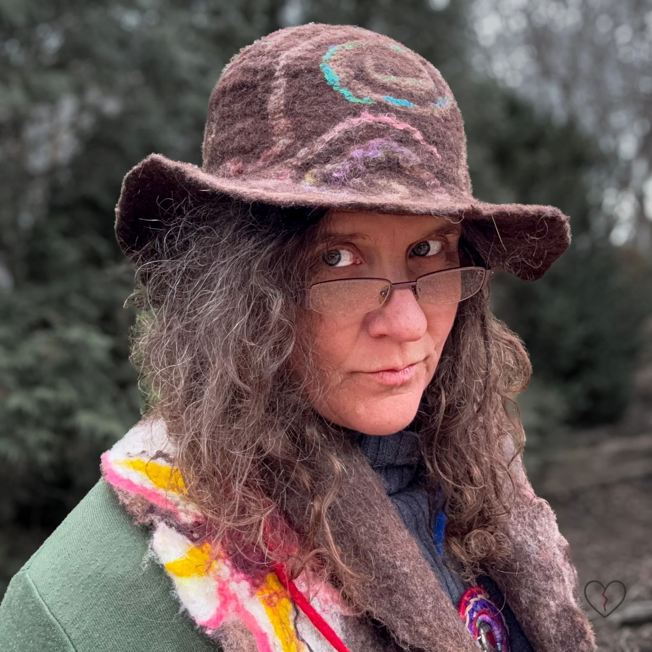 Hand-felted brown wool hat with swirling silk accents displayed on a hat stand outdoors