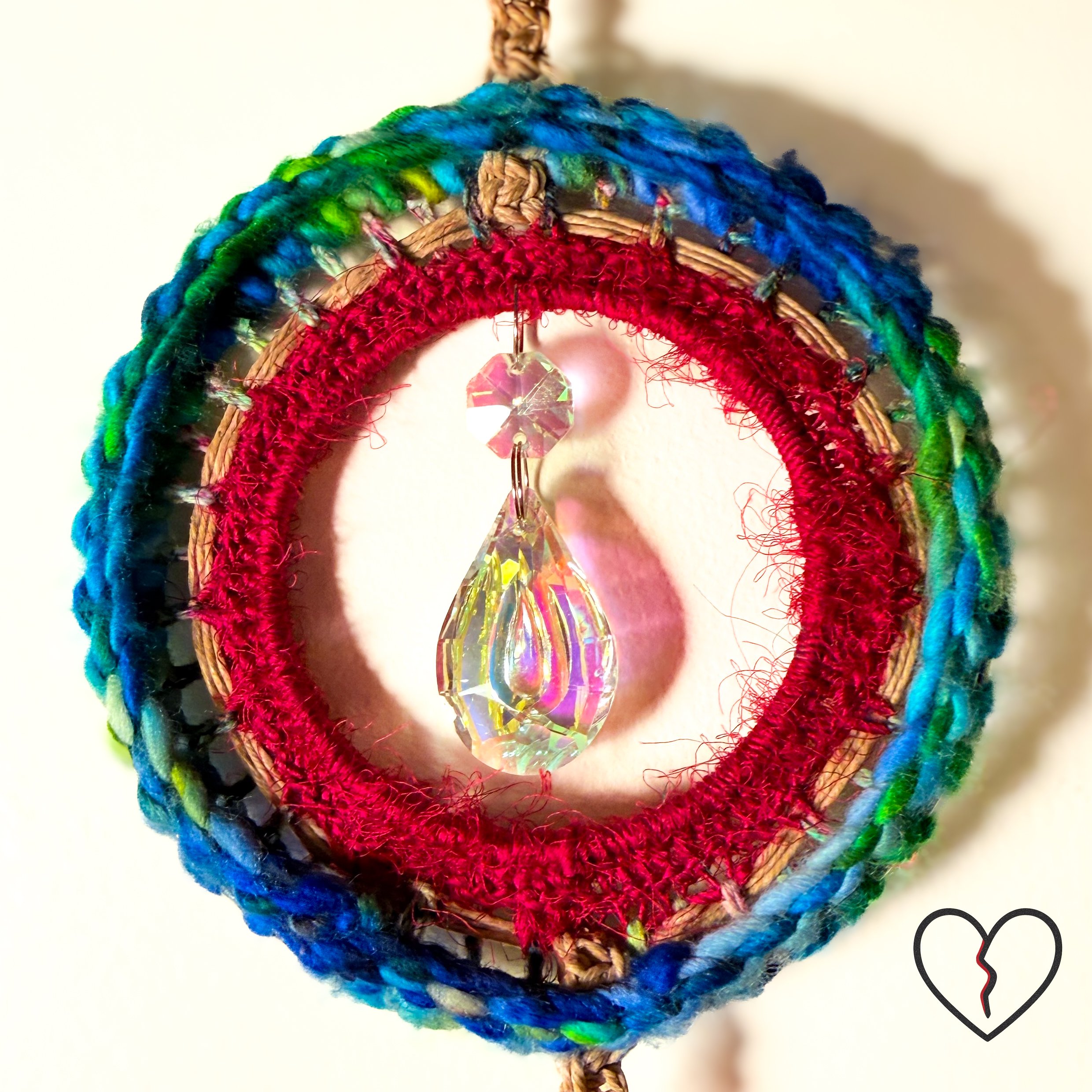 Hand crocheted wool and sari silk dreamcatcher with reclaimed prism and African trade beads representing protection, journey, and illumination. One of a kind fiber wall hanging by Kristi Yapp, 2024.