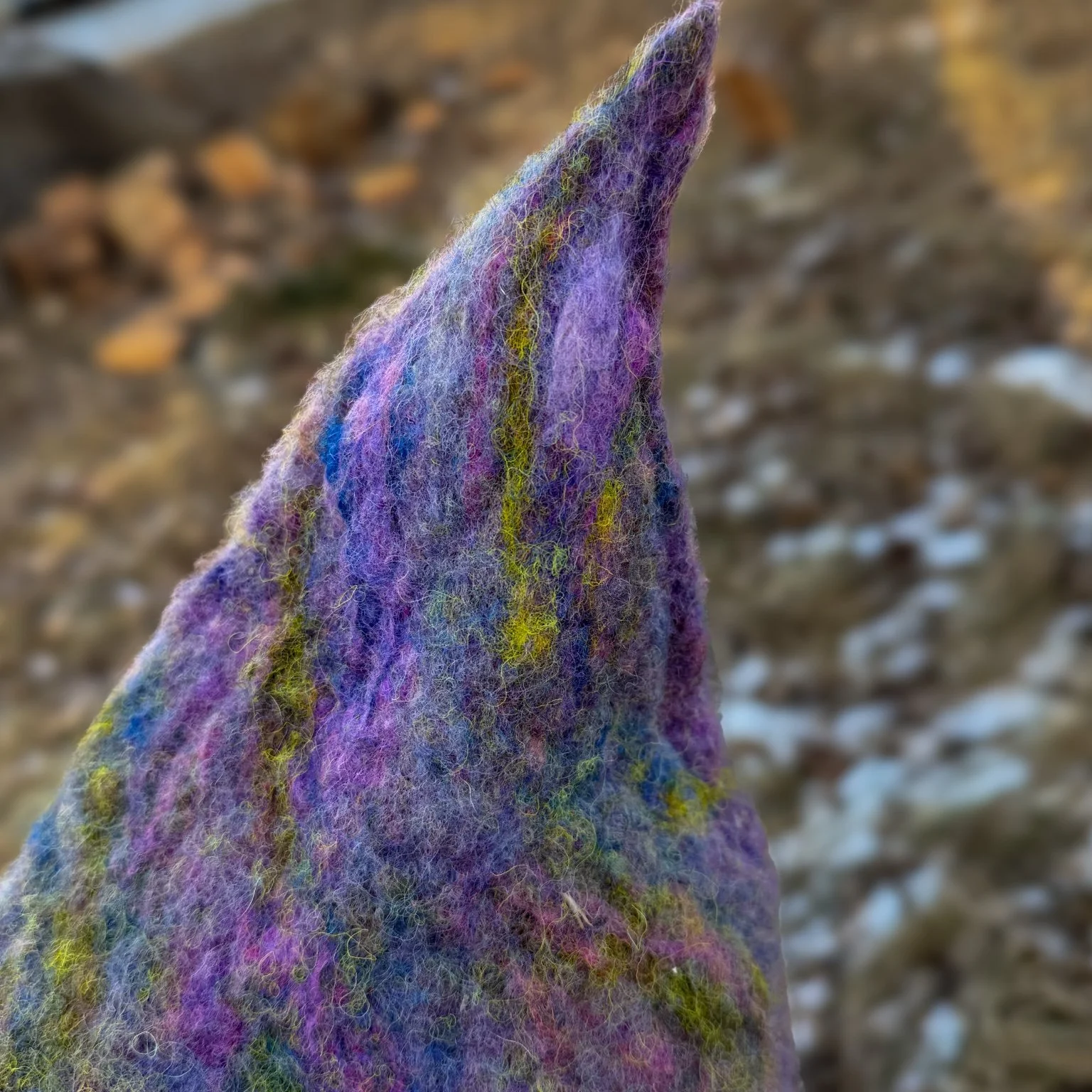 Side view of a hand-felted purple witch hat showing organic shape, layered wool fibers, and slight brim flare.