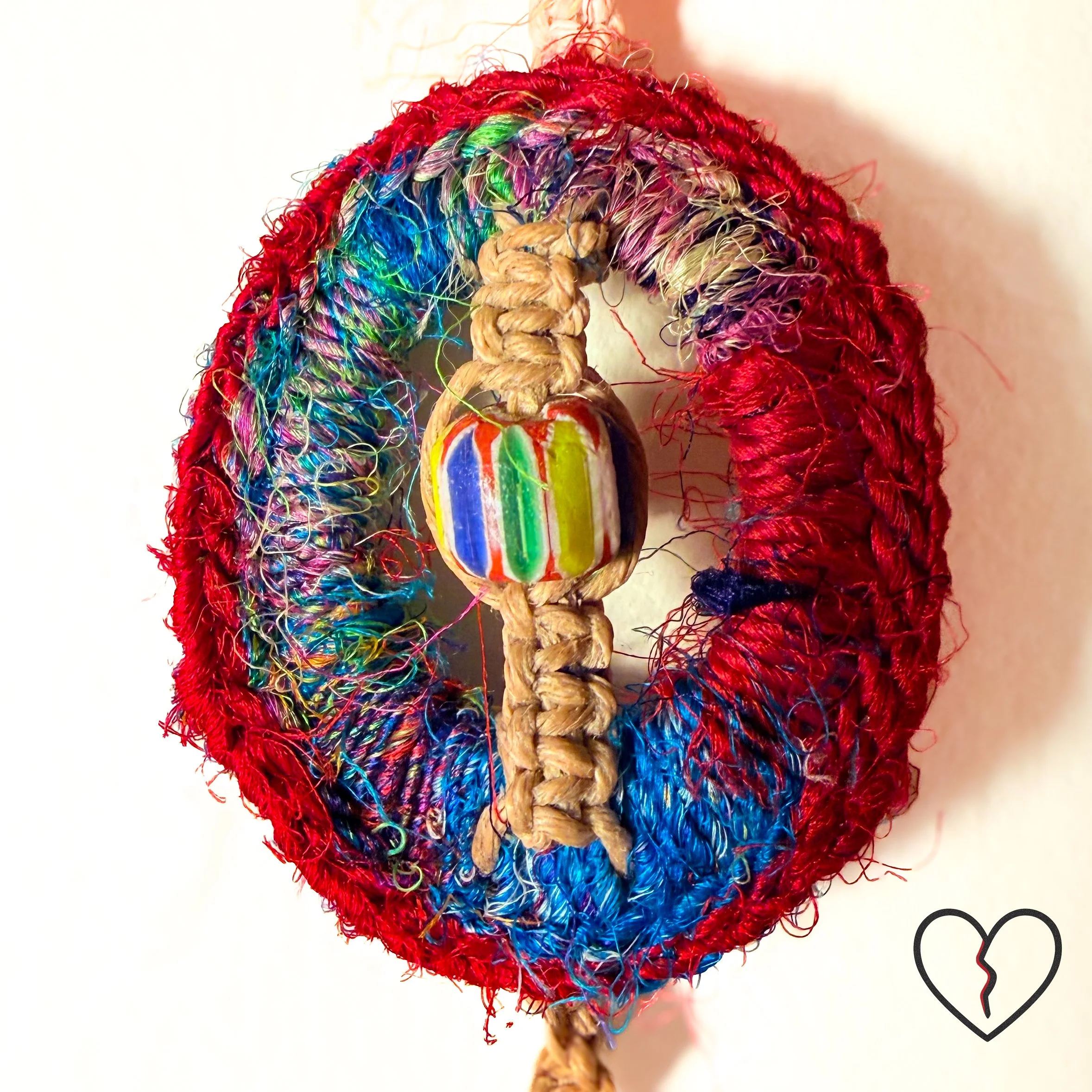 wrapped in sari silk crochet and hemp macrame with glass beads. The piece measures 11 inches long with a 2 inch largest ring and symbolizes triadic balance and transformation.