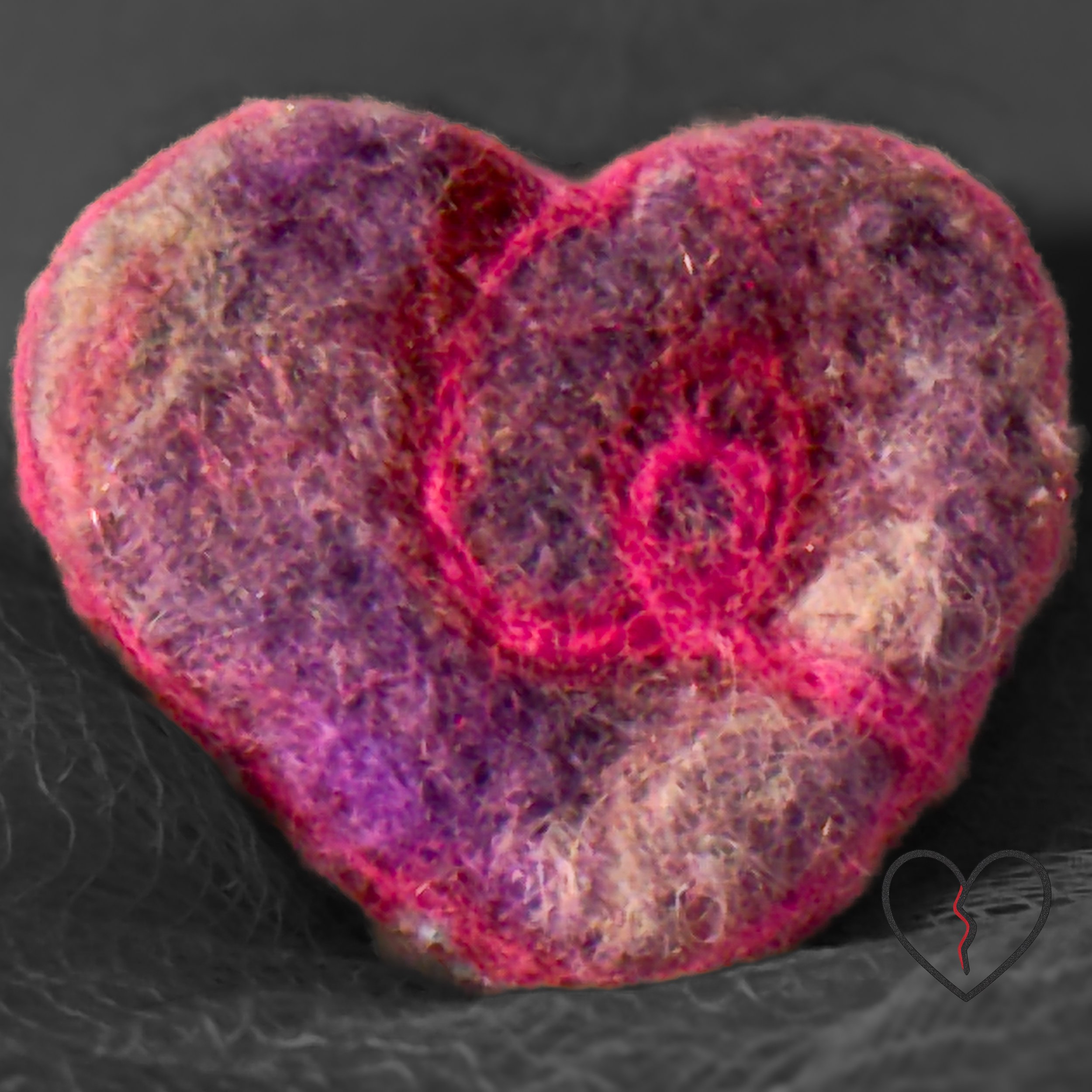 A tiny hand-felted broken heart pin made from hand-dyed purple merino wool with a soft pink wisp. Lightweight, hopeful fiber art by Kristi Yapp – Wool Alchemist.