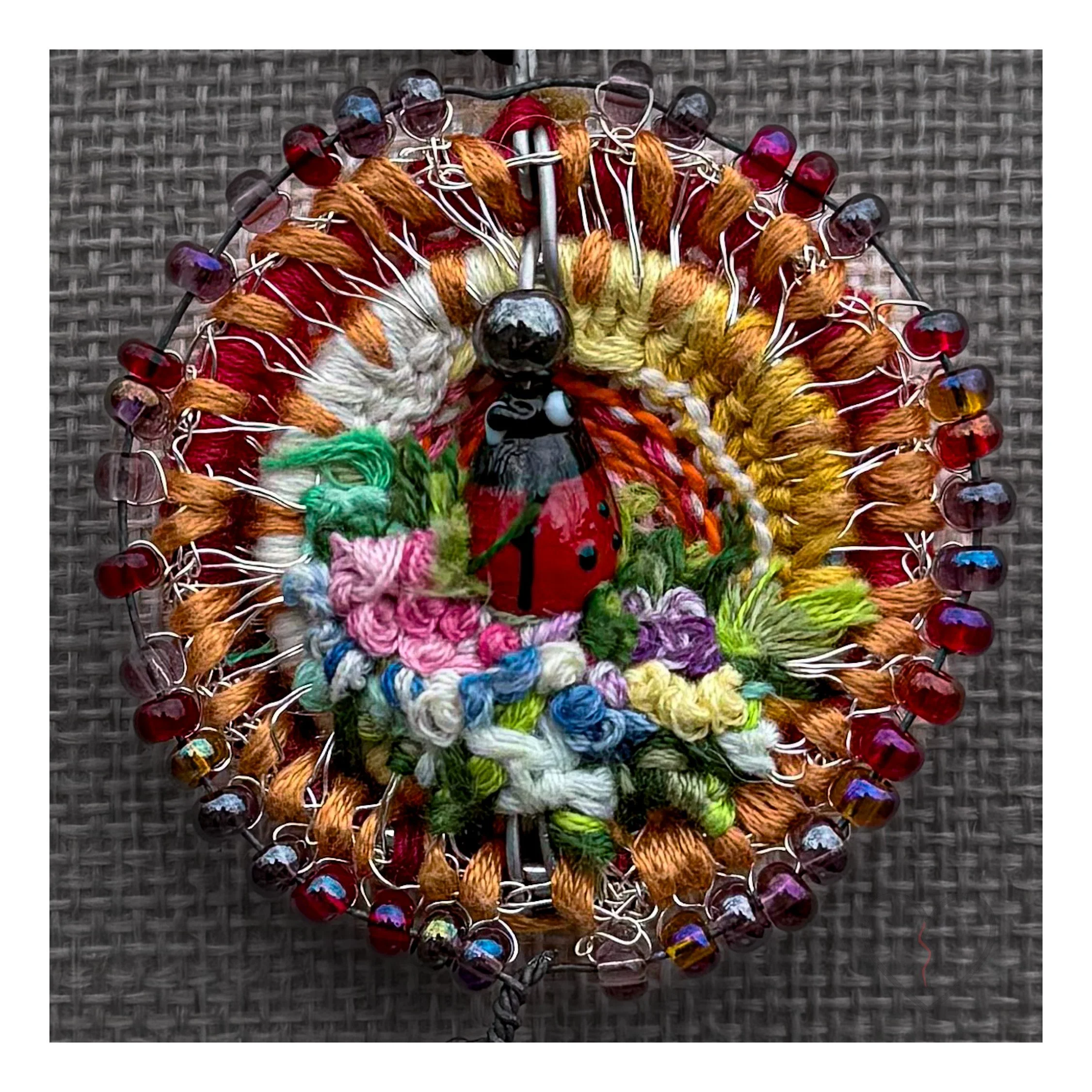 Handmade fiber necklace with jasper hematite and evil eye bead Close up of wool ladybug pendant with textured garden details Circular textile pendant with beadwork and pendulum drop