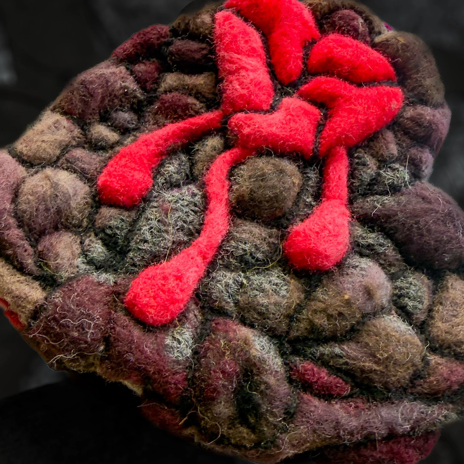 Angled side view of felted broken heart showing raised red scars and layered stone-like wool surface