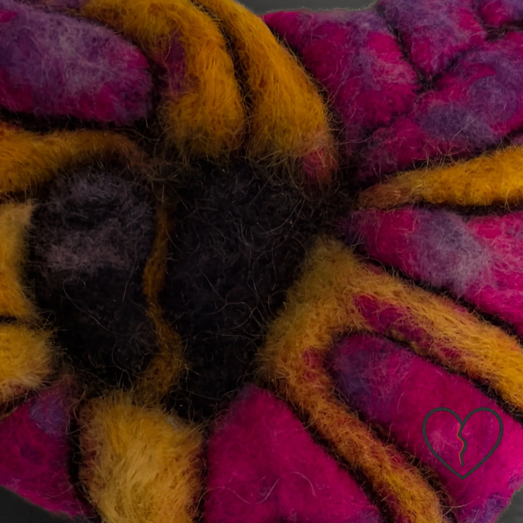 Close-up of textured wool fibers showing flowing cracks and layered color transitions in a broken heart art pin.