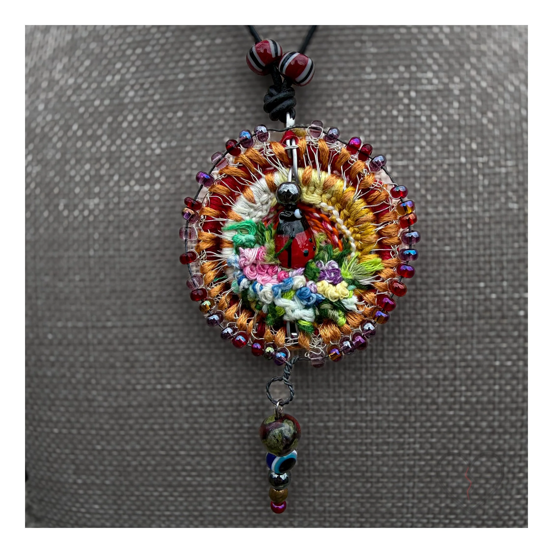 Circular textile pendant with beadwork and pendulum drop