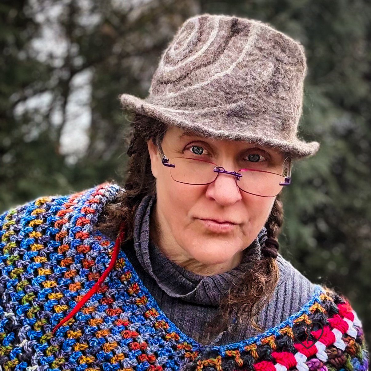 Hand-felted wool fedora hat in natural brown tones with a white and dark brown spiral design, sculptural crown, and short brim, photographed outdoors.
