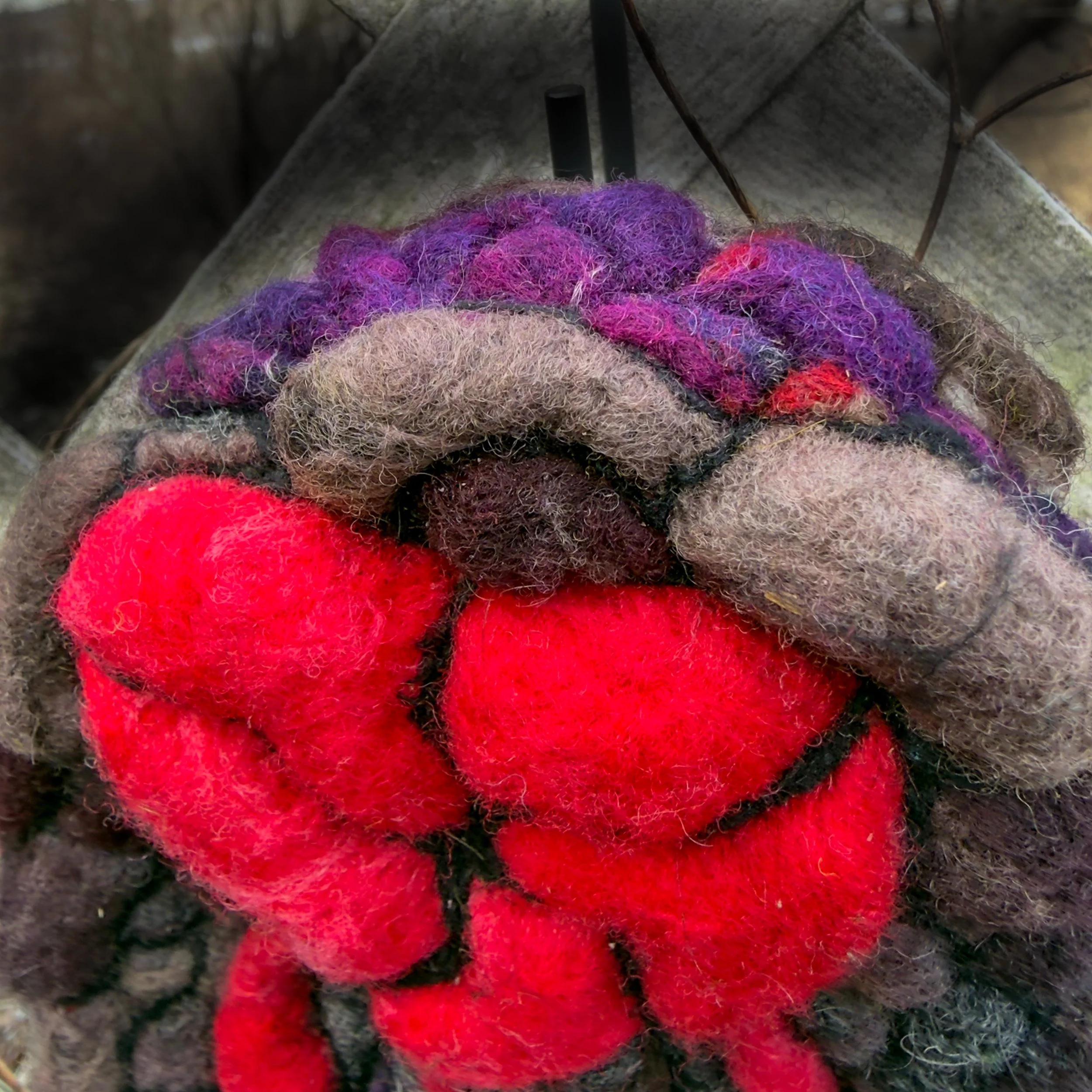 Top view of red felt heart emerging from textured stone-colored wool background