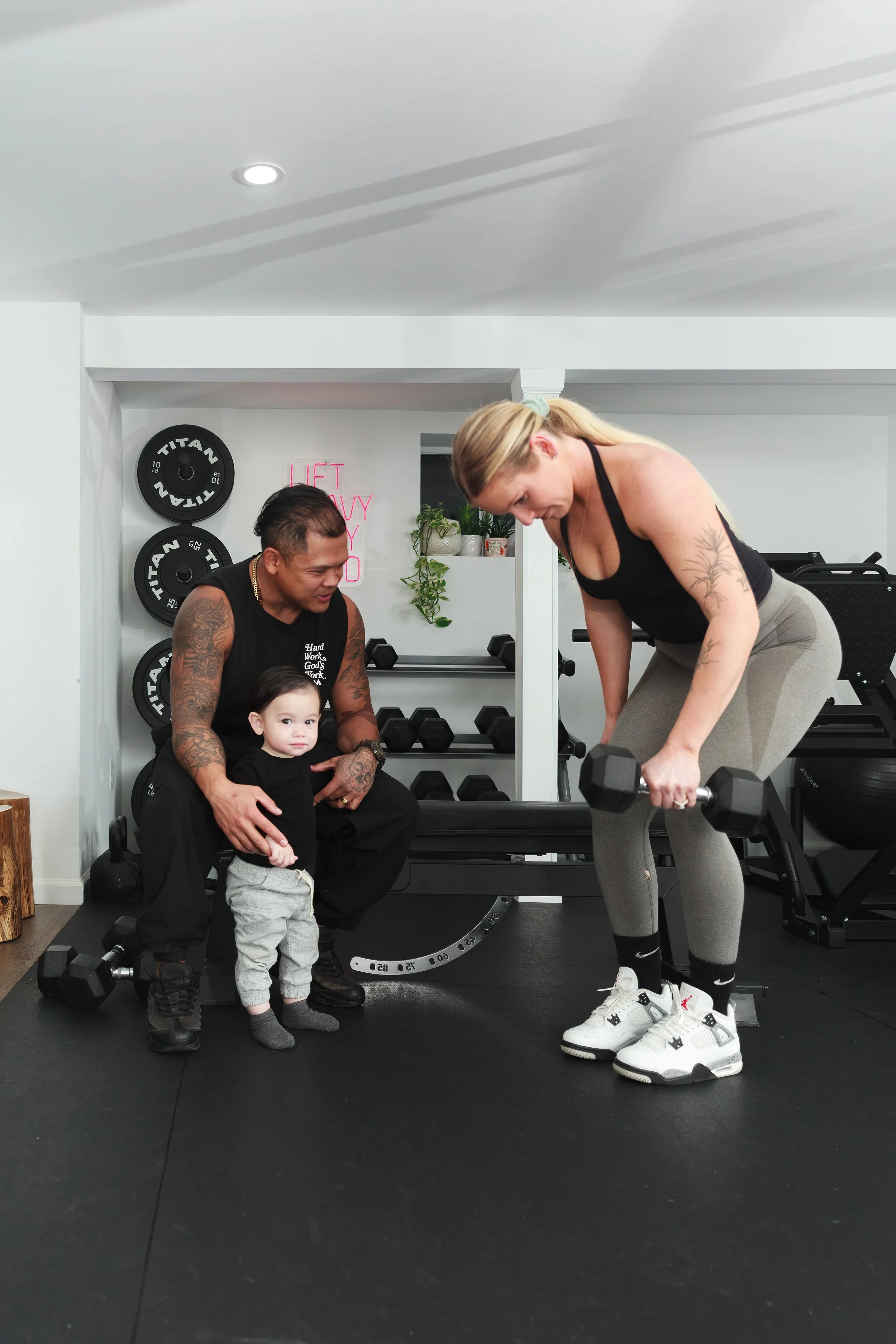 Woman lifting a dumbbell while a man and child watch in a home gym.