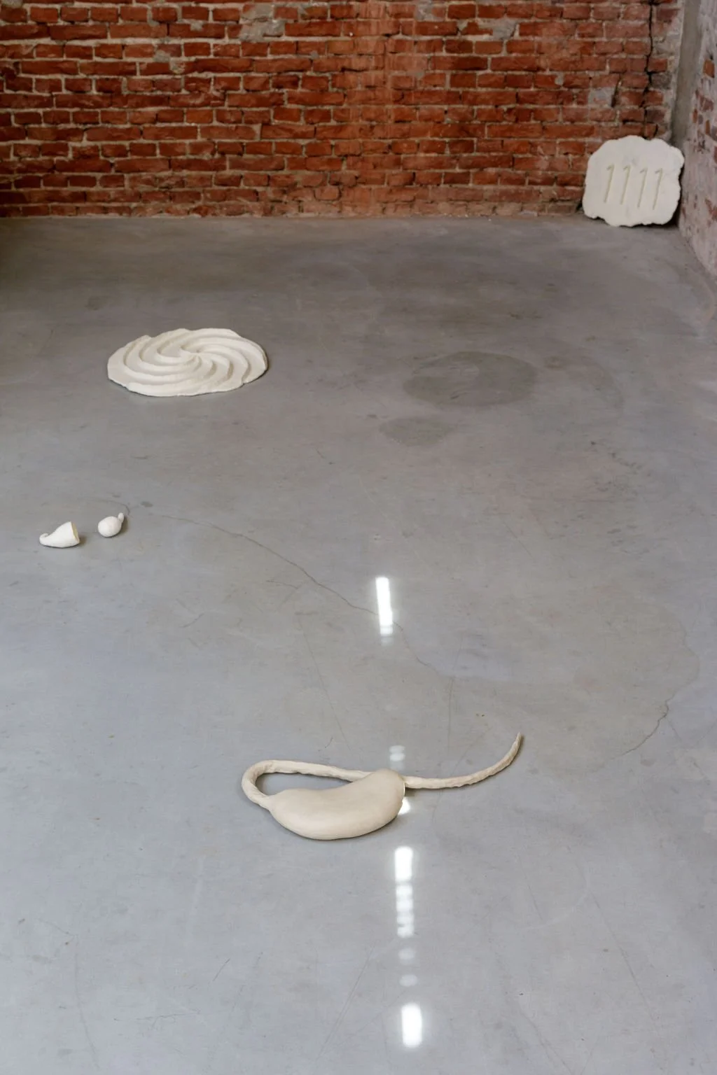 Art installation featuring white, textured, abstract sculptures on a concrete floor against a brick wall background.