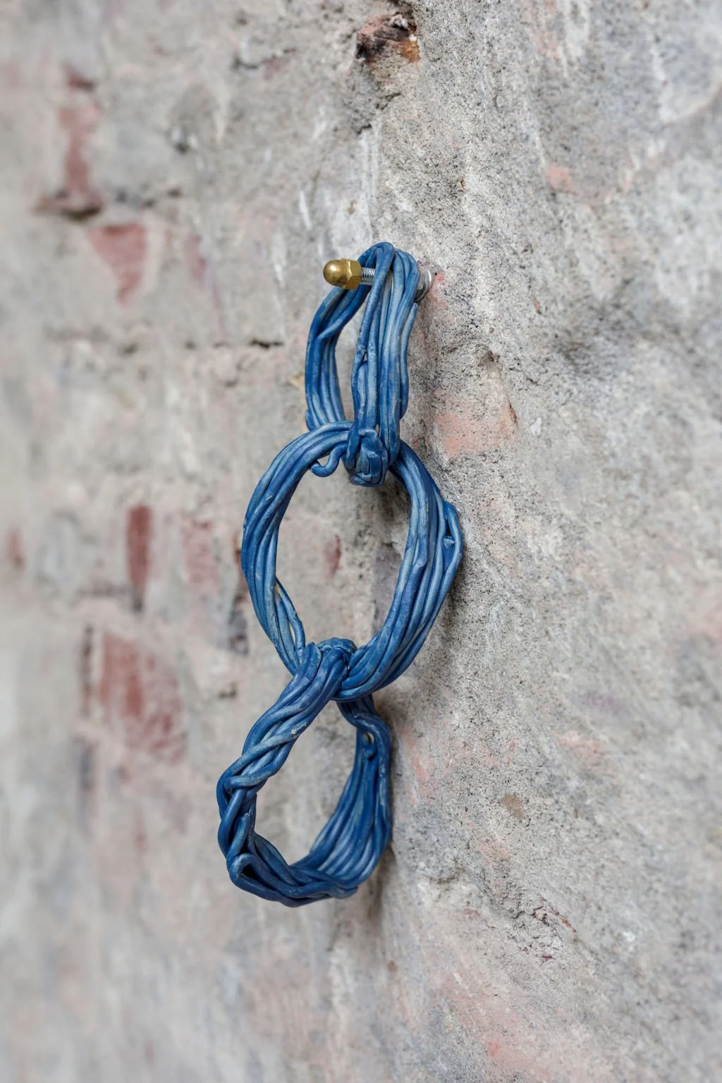 Blue twisted wire looped around a screw on a rough brick wall.