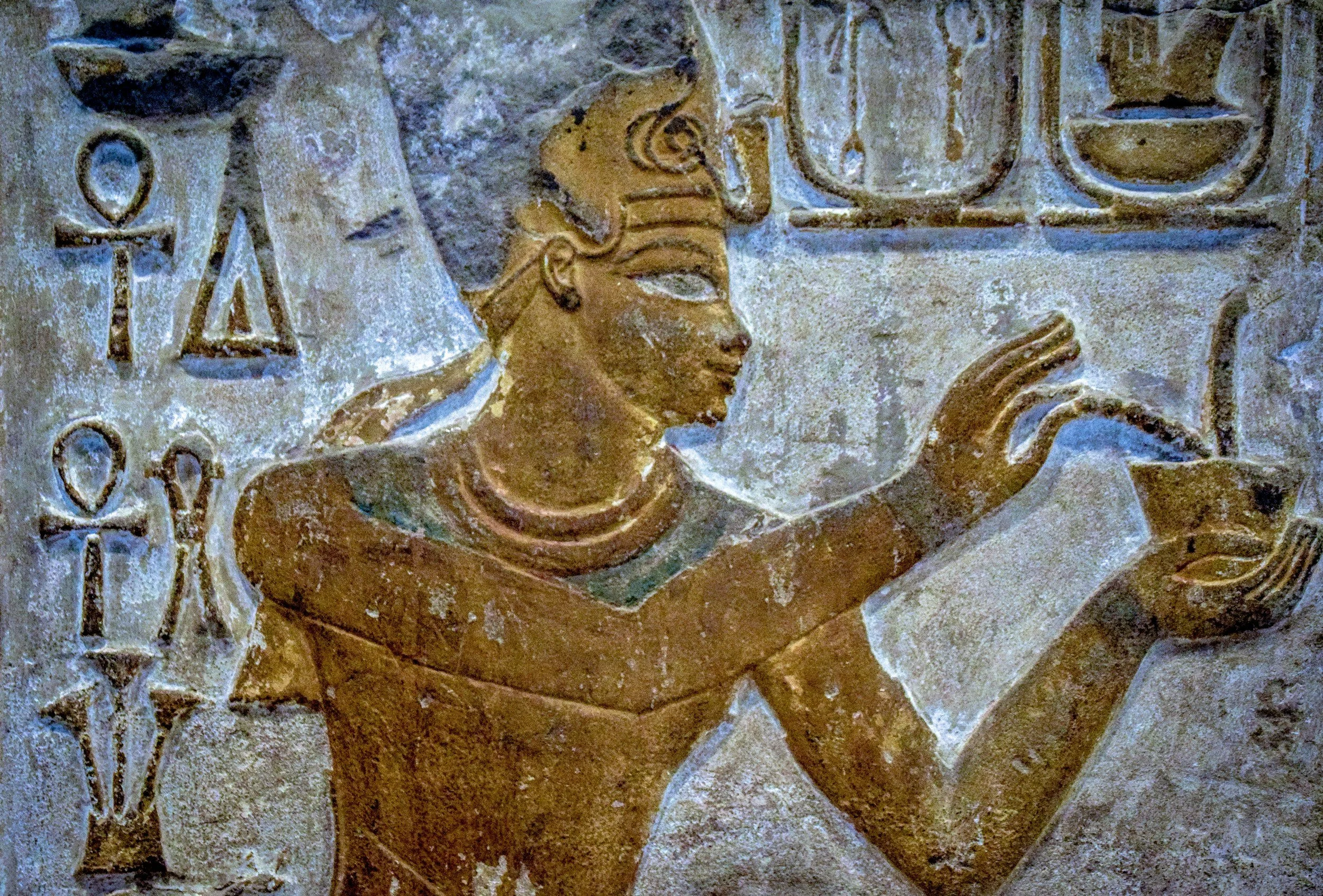 Ancient Egyptian relief showing a woman with jewelry, pointing to hieroglyphs.