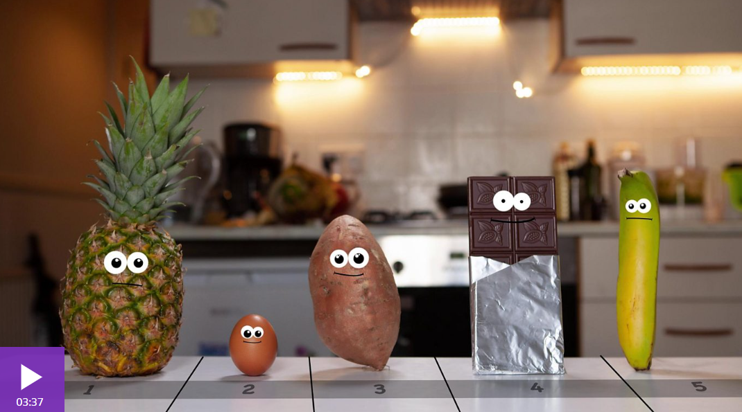 Cartoon faces on a pineapple, egg, sweet potato, chocolate bar, and banana on a numbered table in a kitchen.