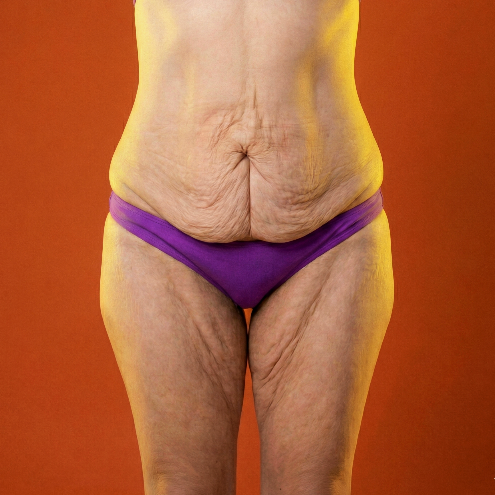 Parte inferior do corpo de uma pessoa idosa usando roupa íntima roxa, com pele enrugada e flácida, contra fundo laranja.