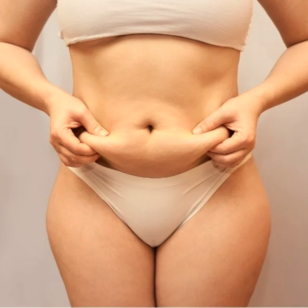 Pessoa segurando a pele da barriga, vestindo roupa íntima bege