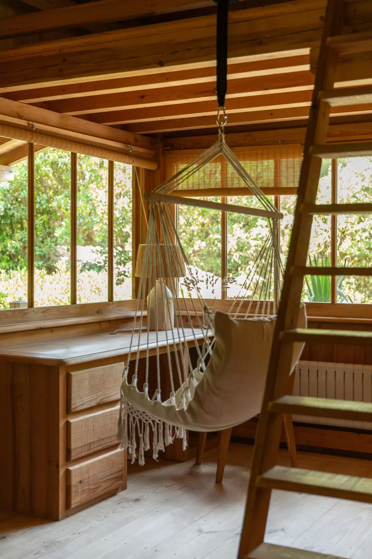 Une pièce en bois avec un bureau, une lampe, une balançoire en tissu suspendue et une échelle en bois
