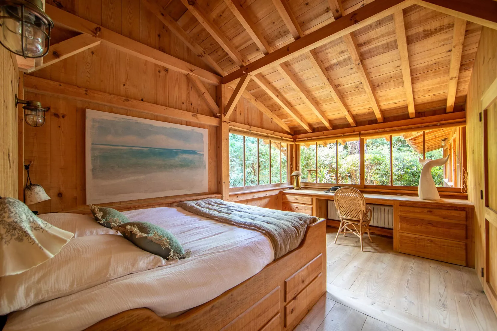 Chambre en bois avec grand lit, bureau et vue sur la nature à travers de grandes fenêtres