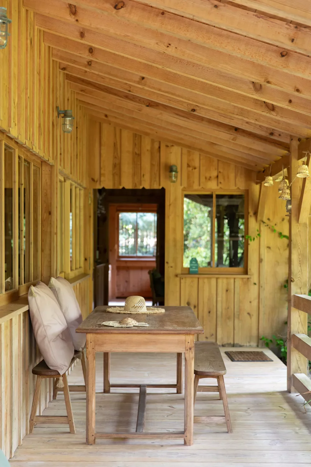 Terrasse en bois avec table, banc et chaises, intérieur d'une maison en bois, vue sur un jardin, décoration simple et chaleureuse.