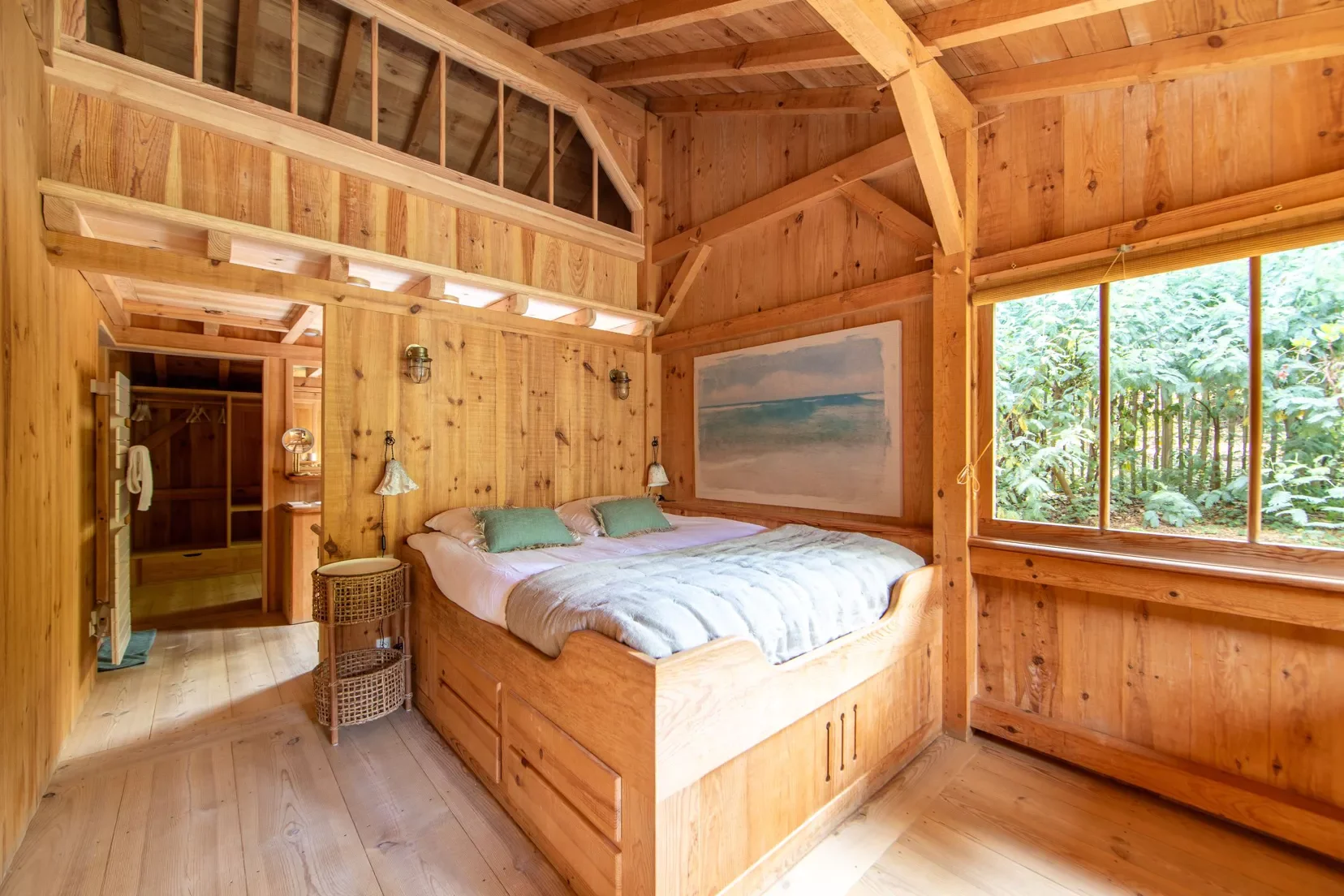 Chambre en bois avec lit double, vue sur la végétation extérieure par une grande fenêtre