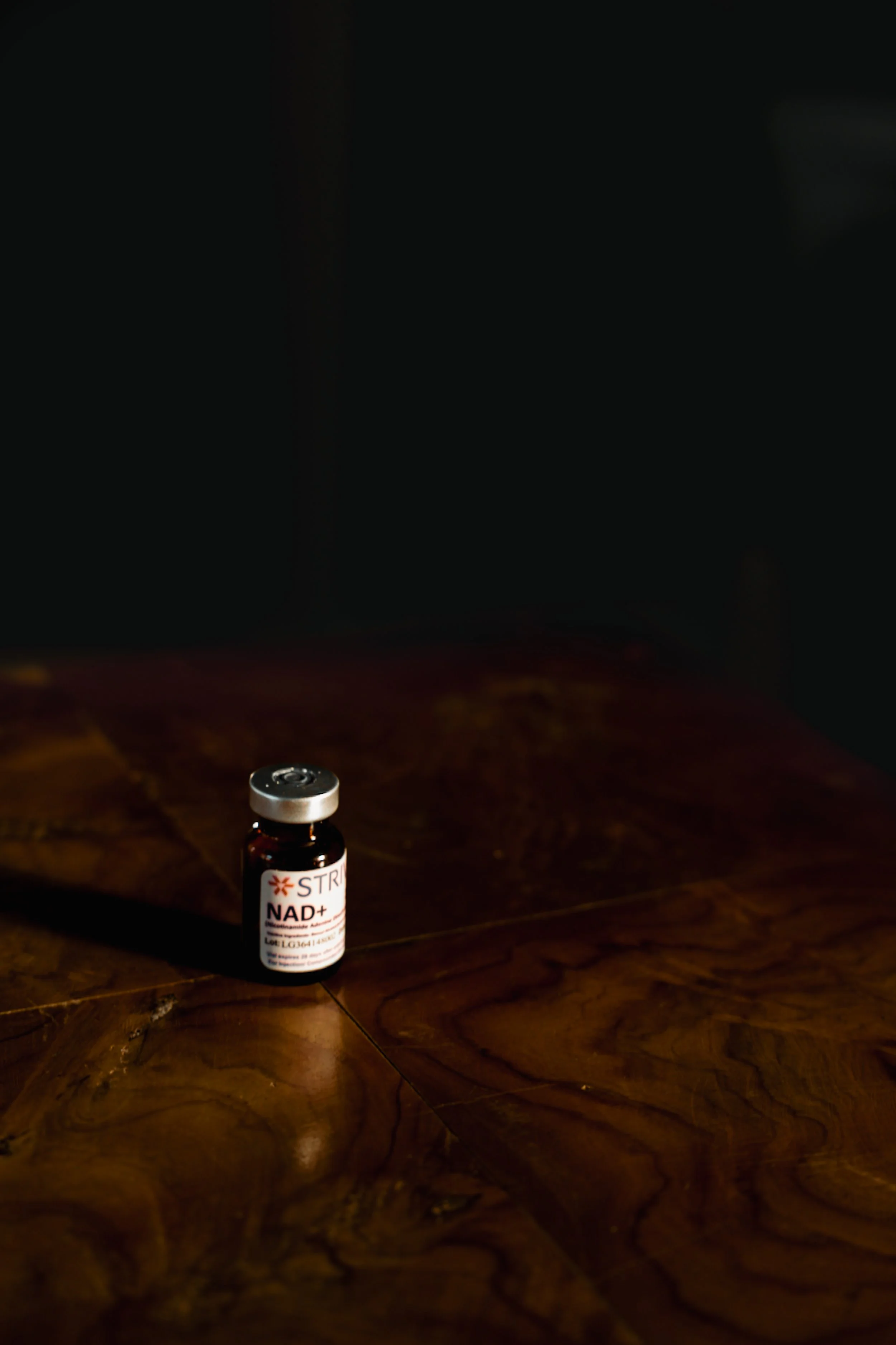 A small brown glass vial labeled 'NAD+' sits on a dark wooden surface with a black background.