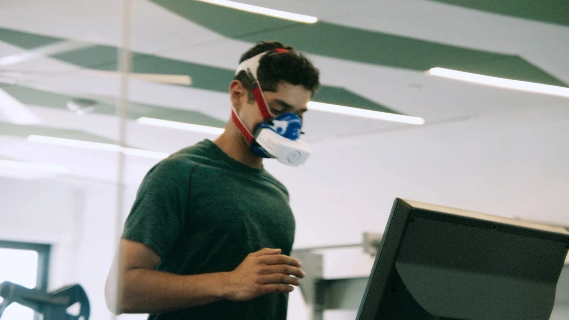 Woman on a treadmill wearing a mask connected to a machine in a medical or research setting.