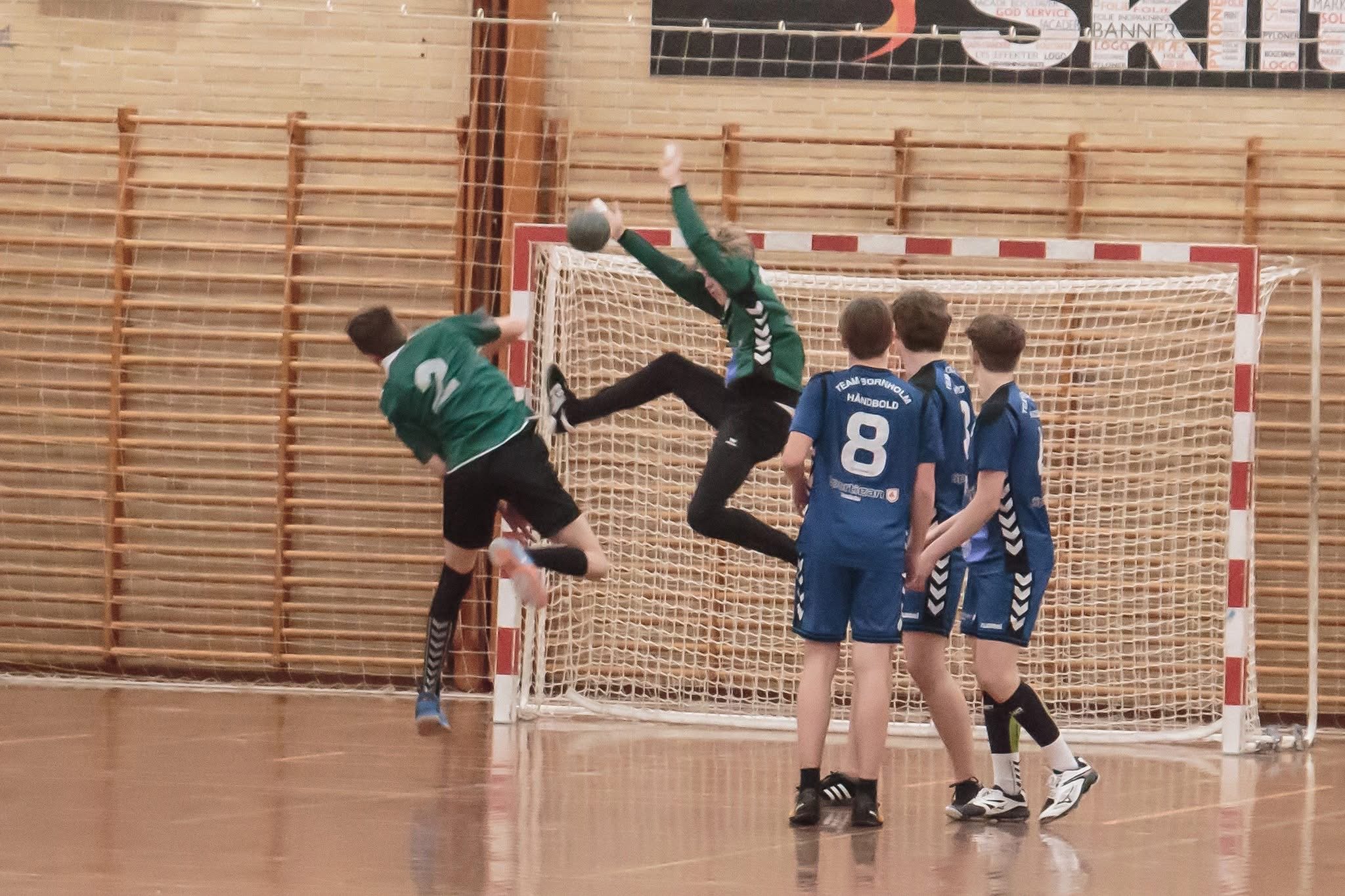 Udløser et håndboldskud foran mål, hvor målmand og flere spillere ser ud til at forsøge at blokere skuddet.