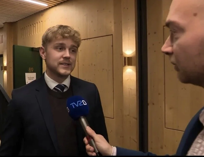 To mænd i forretningspåklædning i en samtale. Den ene mand holder en mikrofon med TV2 logoet.