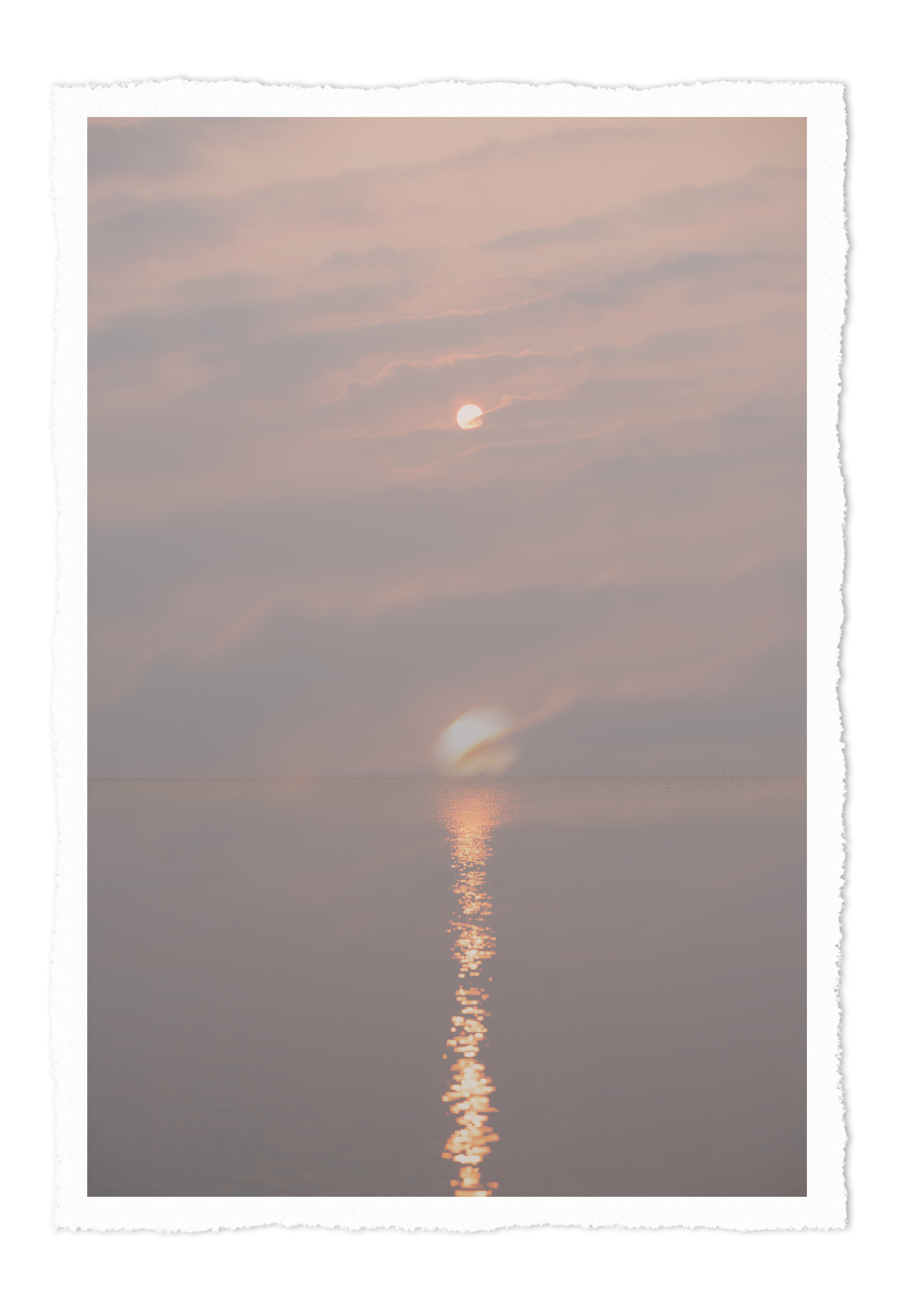 Sun partially obscured by clouds over a calm body of water during sunset.