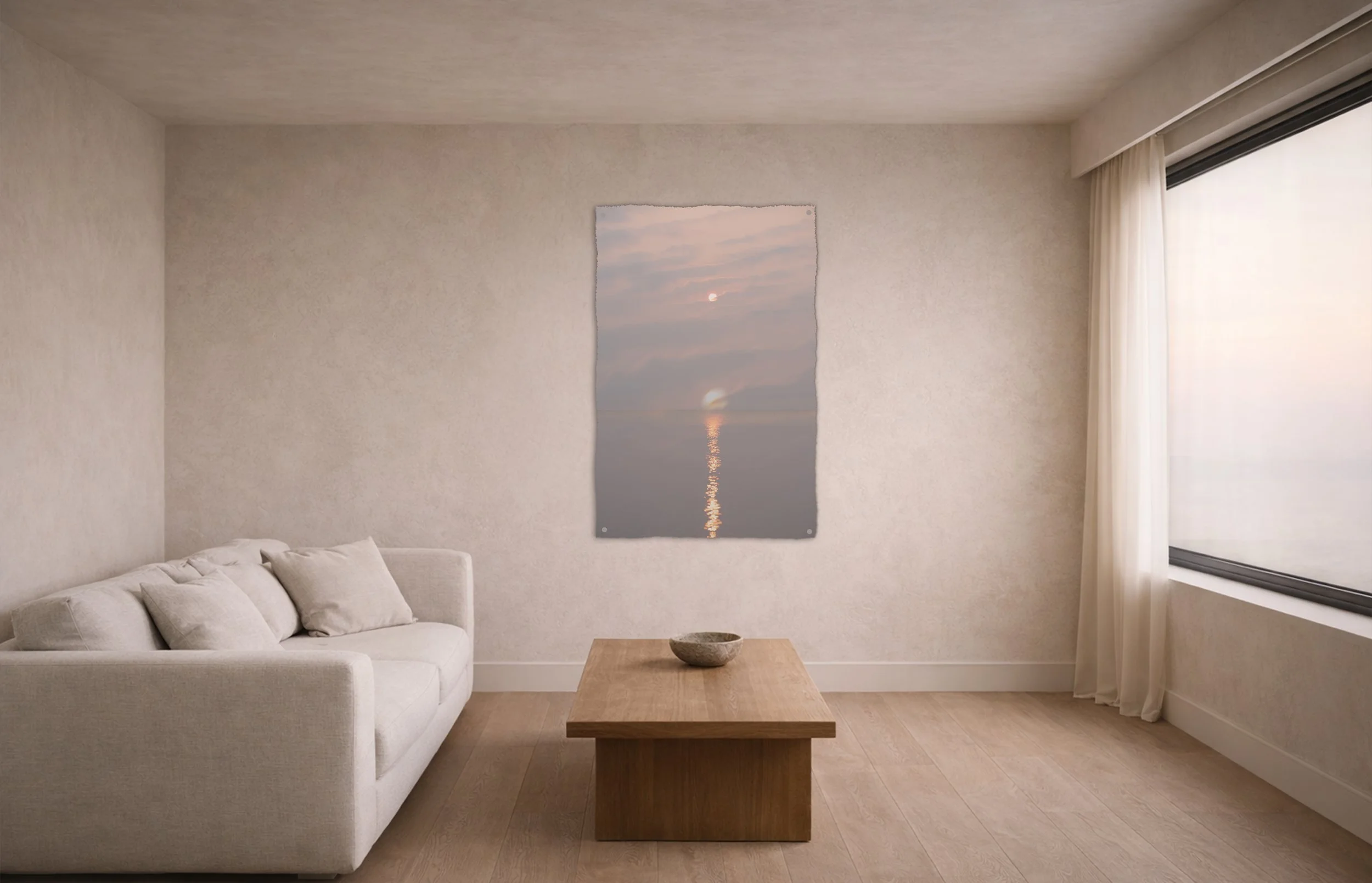 Minimalist living room with a white sofa, a wooden coffee table with a decorative bowl, and a large window with sheer curtains. There is a wall art piece depicting a sunset over the water.