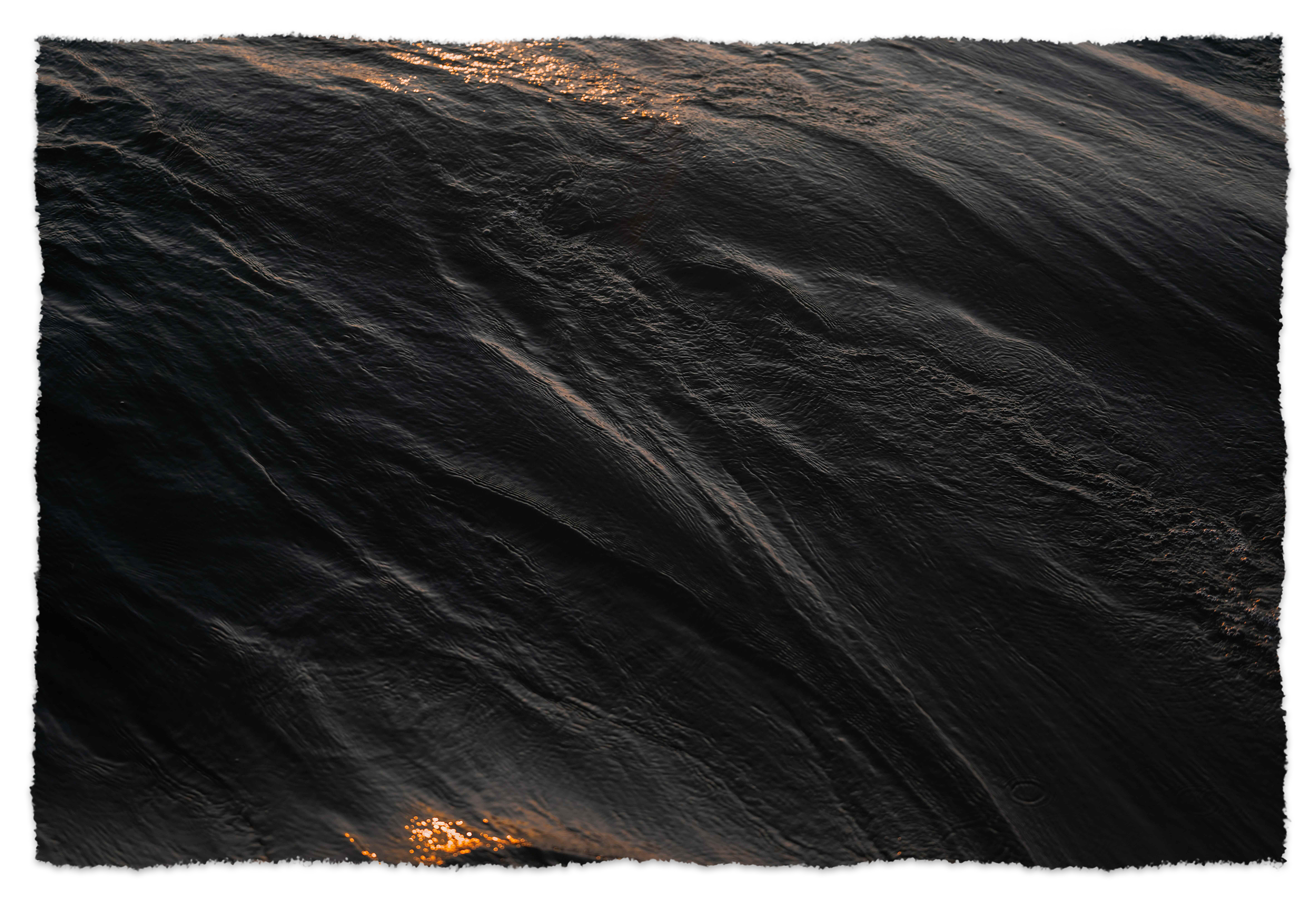 Close-up of dark, textured water surface with ripples, reflecting light at sunset or sunrise.