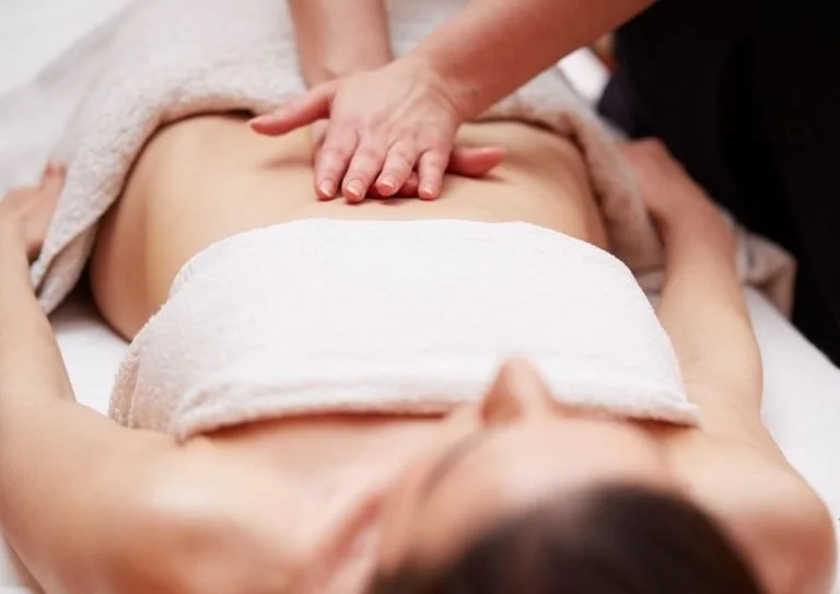Une personne recevant un massage sur le ventre, allongée sur une table de massage.