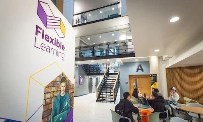 A poster for the flexible learning programme at the University of Manchester outside a brightly lit atrium