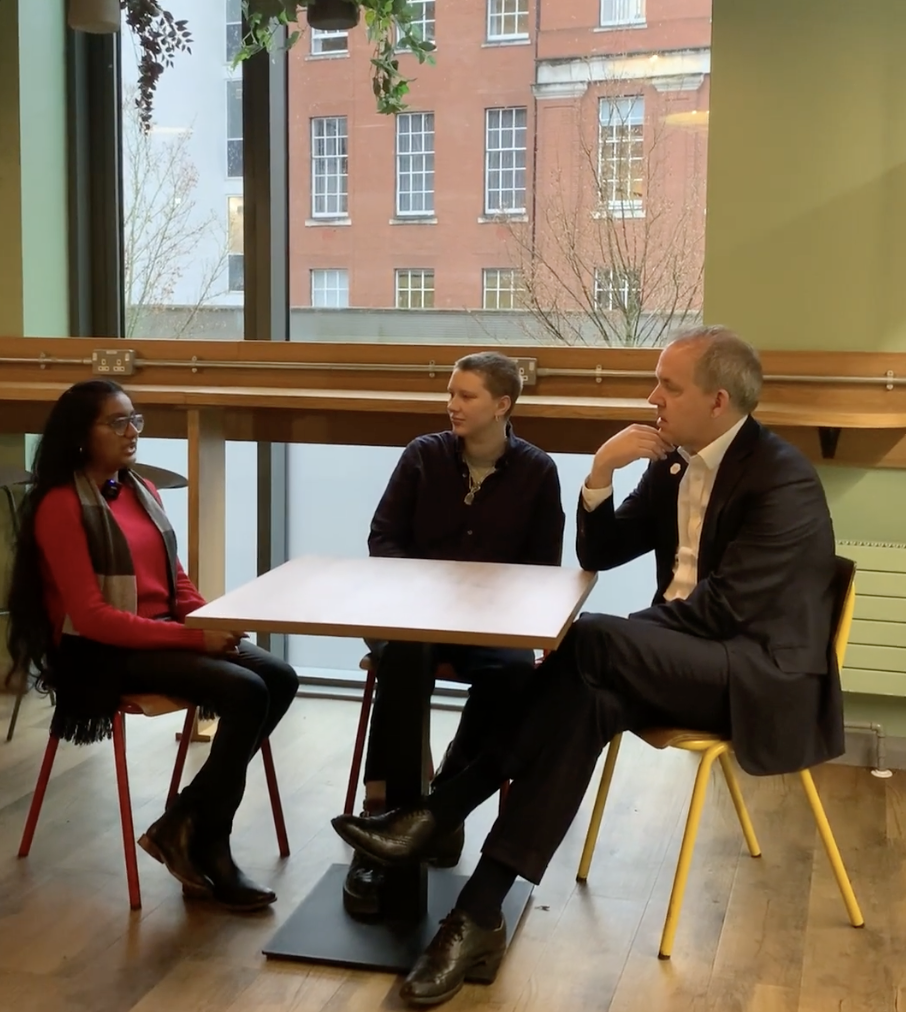 Professor Duncan Ivison in conversation with two students in a cosy cafe