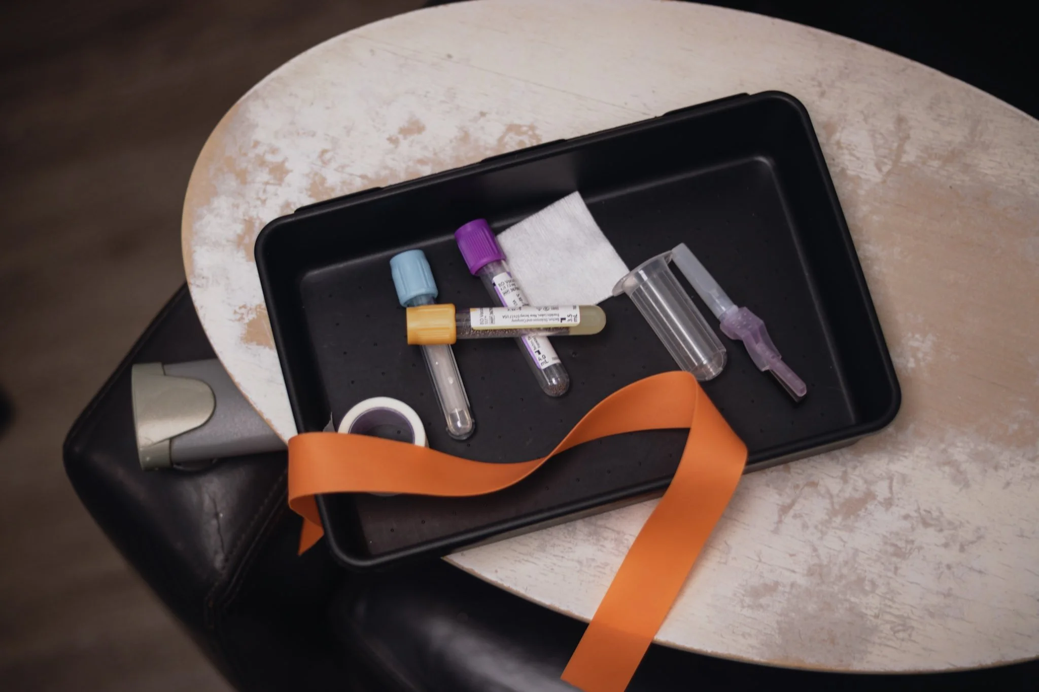 A tray containing medical testing supplies such as test tubes, a dropper, and a piece of gauze, placed on a wooden table.