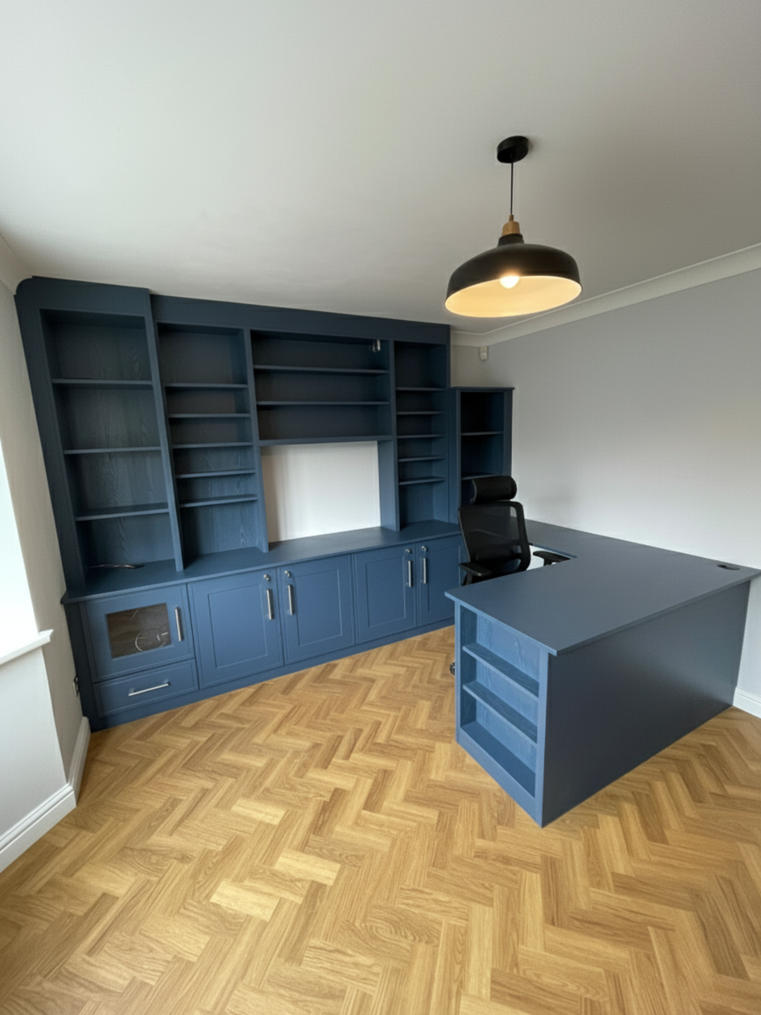 Custom blue home office with integrated shelving, storage cabinets and L-shaped desk by Eldwick Interiors.