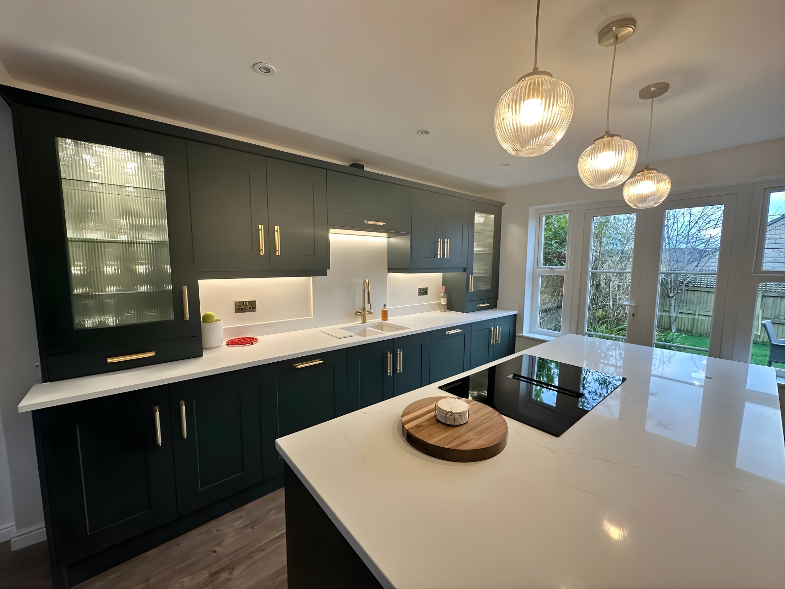 Modern dark green kitchen with gold handles, fluted glass cabinets and white quartz worktops, designed by Eldwick Interiors.