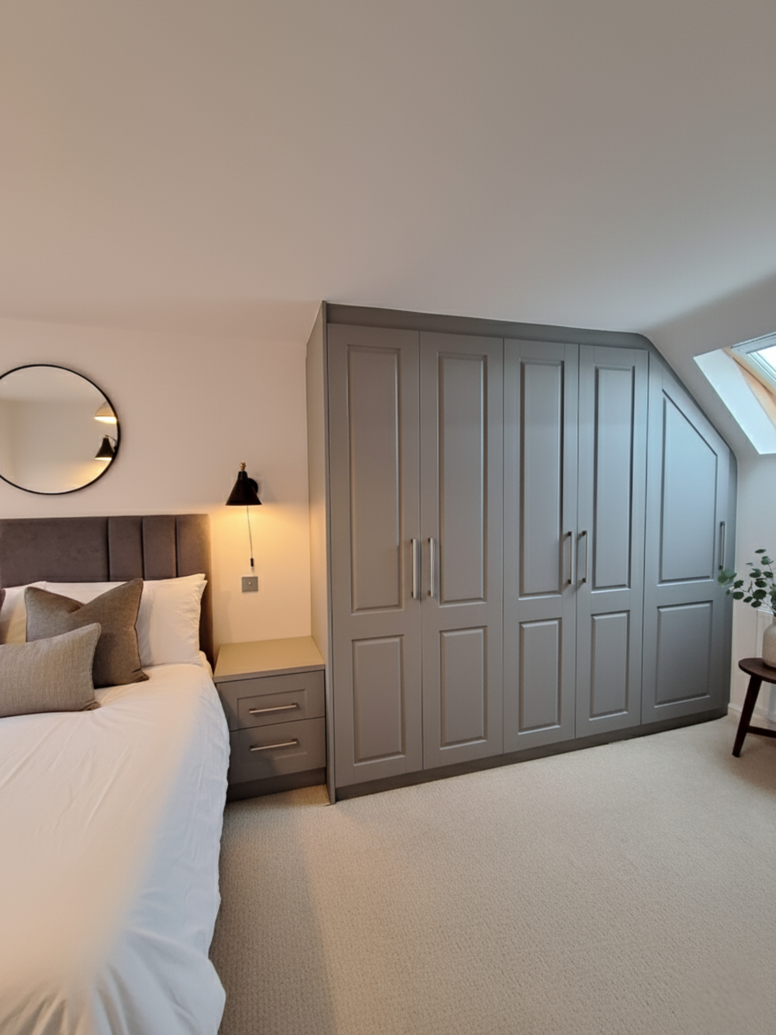 Custom grey fitted wardrobes designed for a sloped ceiling, with seamless shaker doors in a contemporary bedroom by Eldwick Interiors.