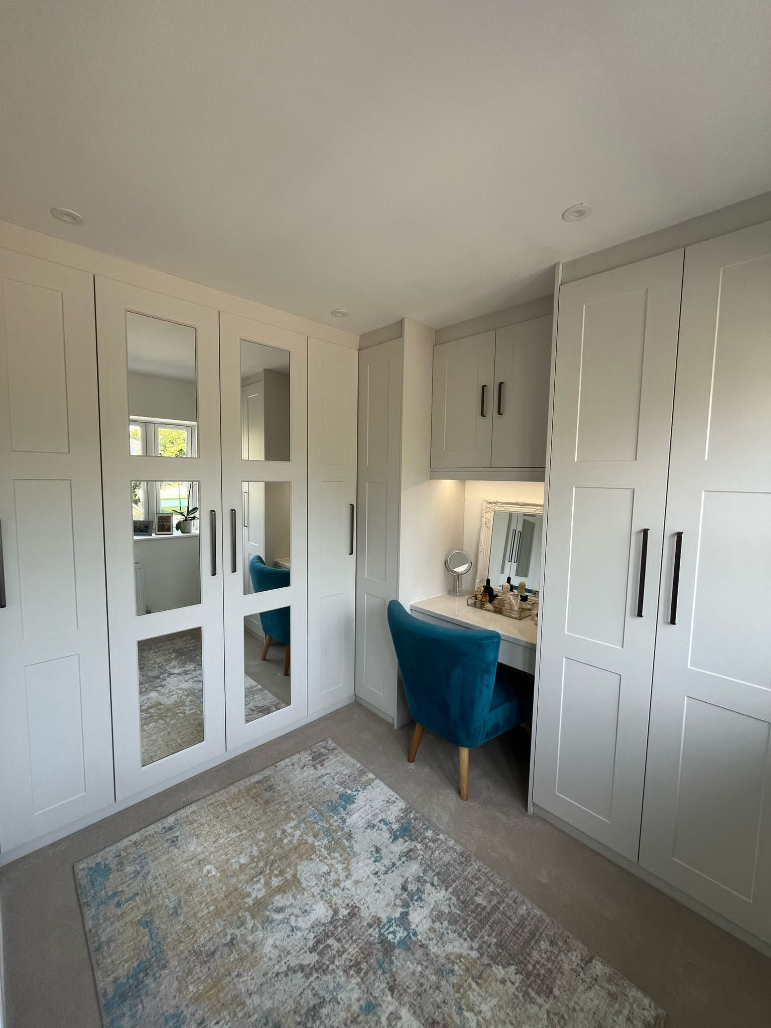 Custom grey fitted wardrobes with full-height mirrored doors and a built-in dressing table, designed by Eldwick Interiors.